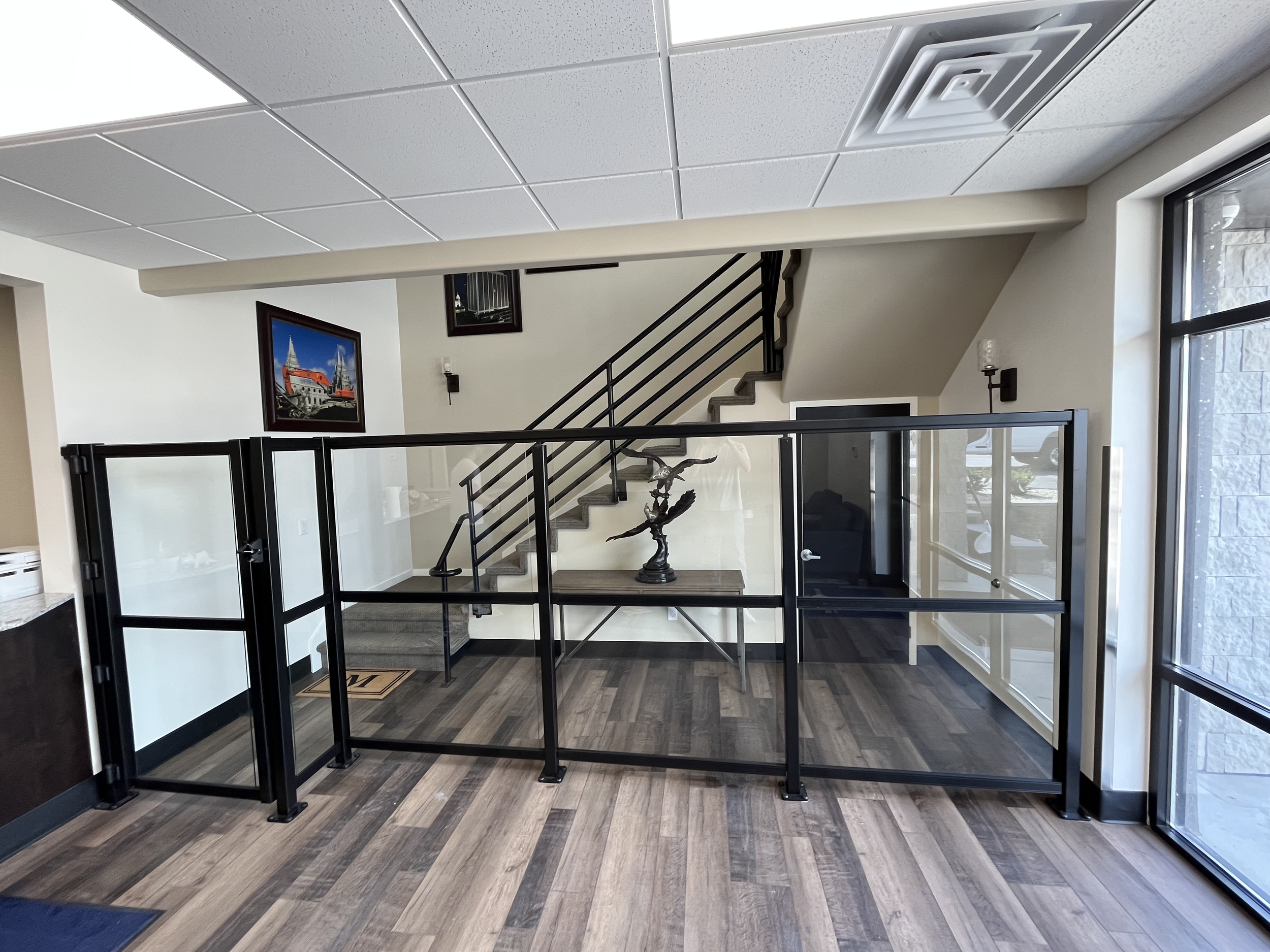 Interior view of a modern office or lobby with a staircase, decorative sculpture, framed pictures on the wall, large window, and glass railing.