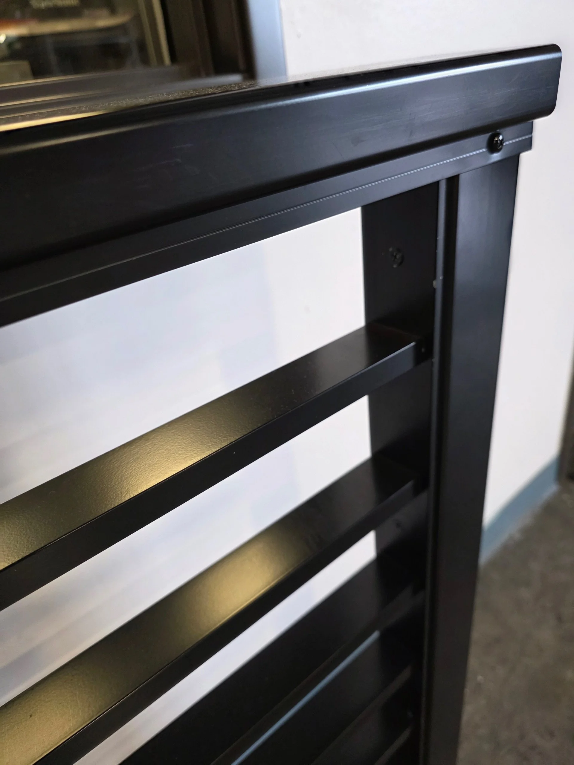 Close-up of a black wooden piece of furniture, possibly a music stand or a shelf, with a bolt visible on the right side, against a plain wall.