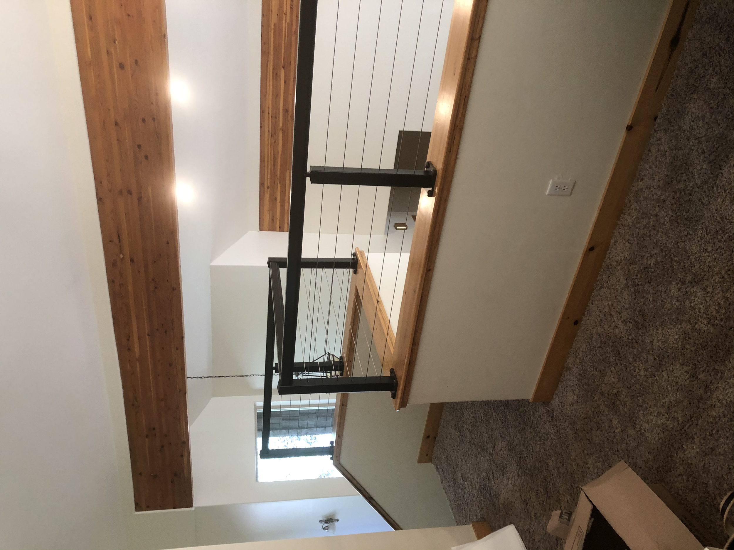 Interior of a house with a wooden railing, drywall walls, a ceiling with wooden beams, and carpeted floor.