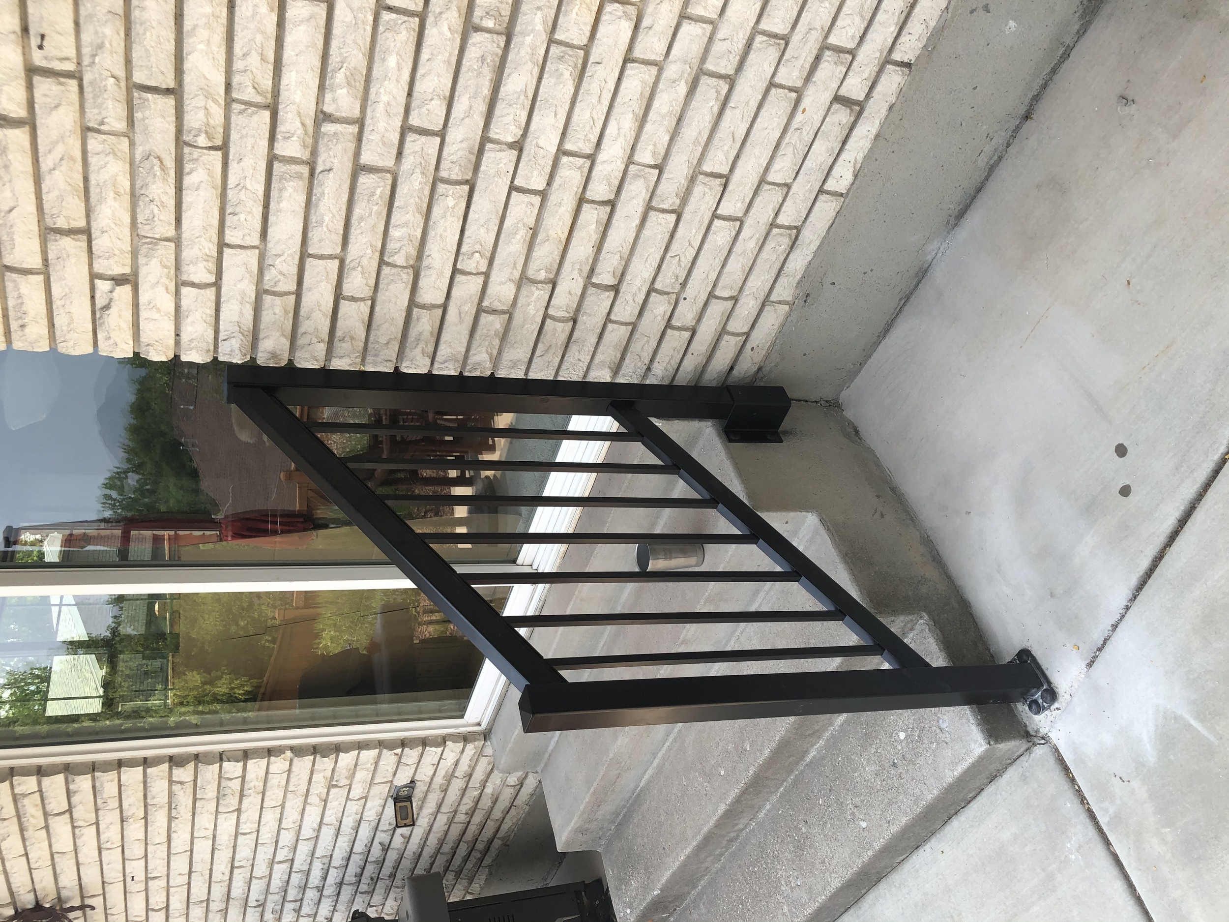 A small set of concrete steps with a black metal railing outside a house with beige brick siding and a sliding glass door.