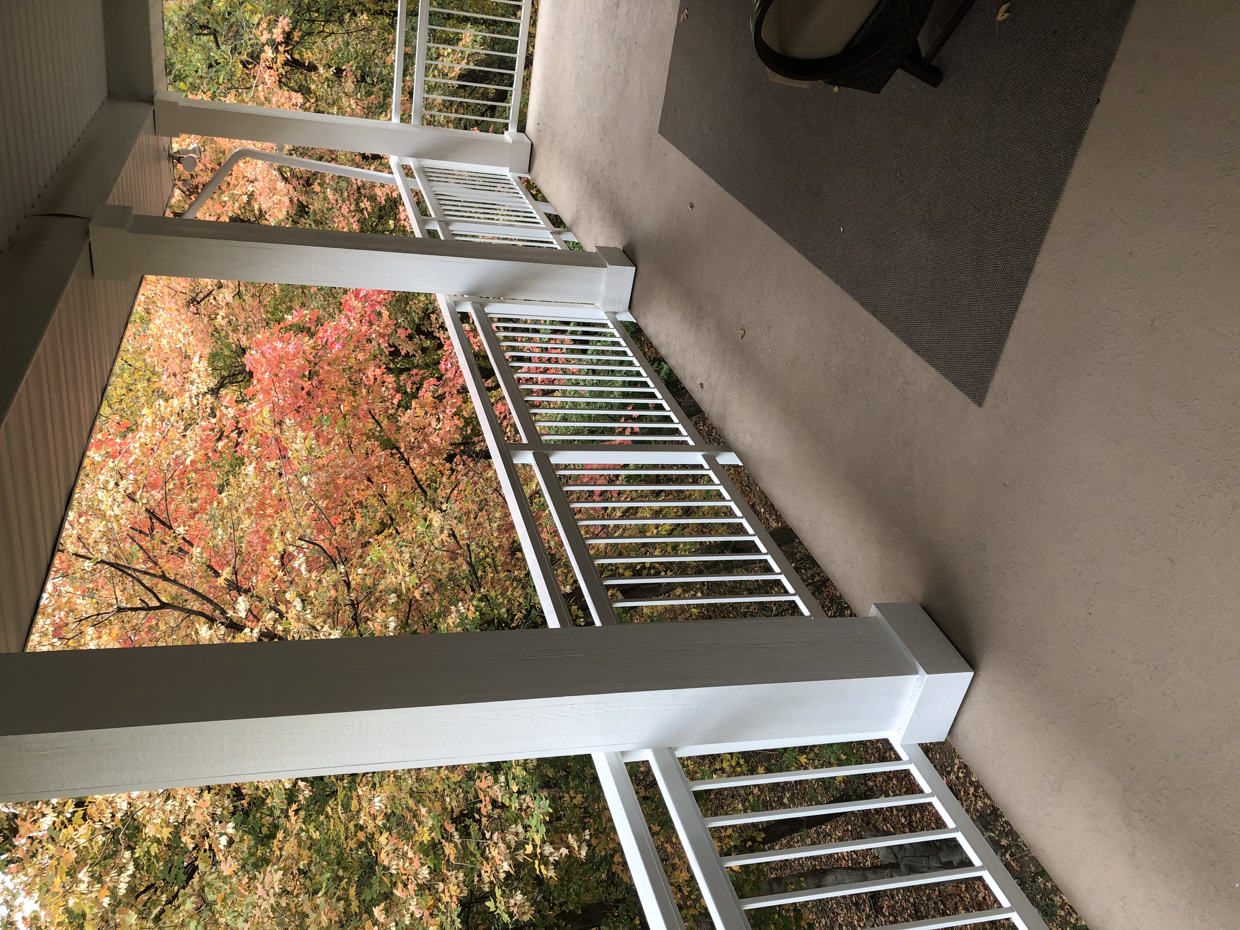 View of a balcony with white railing overlooking trees with autumn-colored leaves.