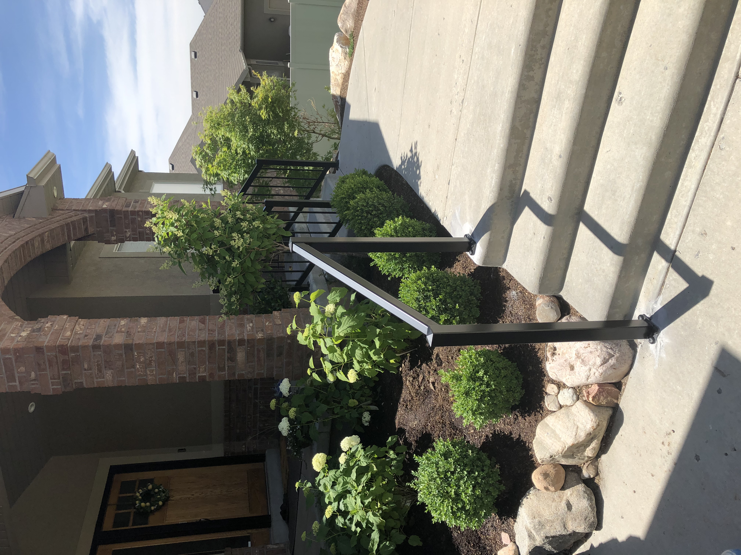 Concrete steps leading to the front door of a house with brick pillars, greenery, and a clear blue sky.