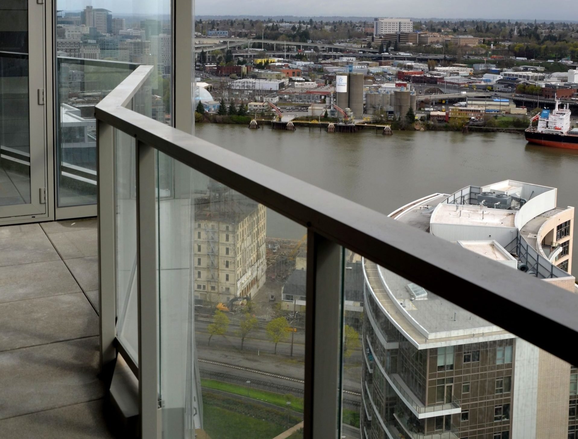 View from a tall building showing the city skyline, river, bridges, industrial area, and a ship docked along the riverbank.
