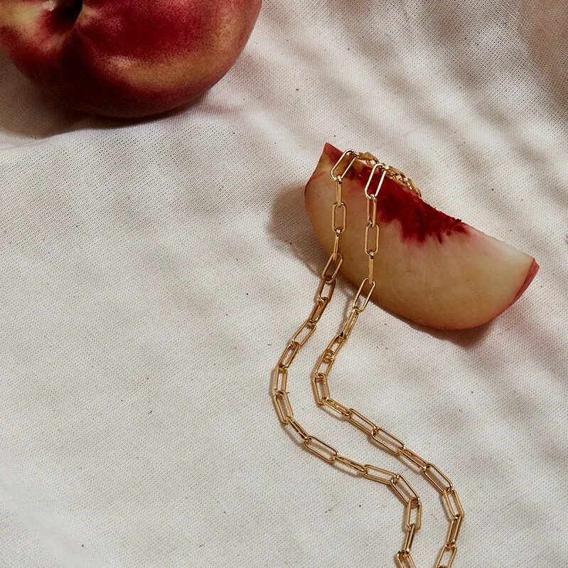 A sliced apple with a chain draped over it and a whole apple in the background on a white surface.