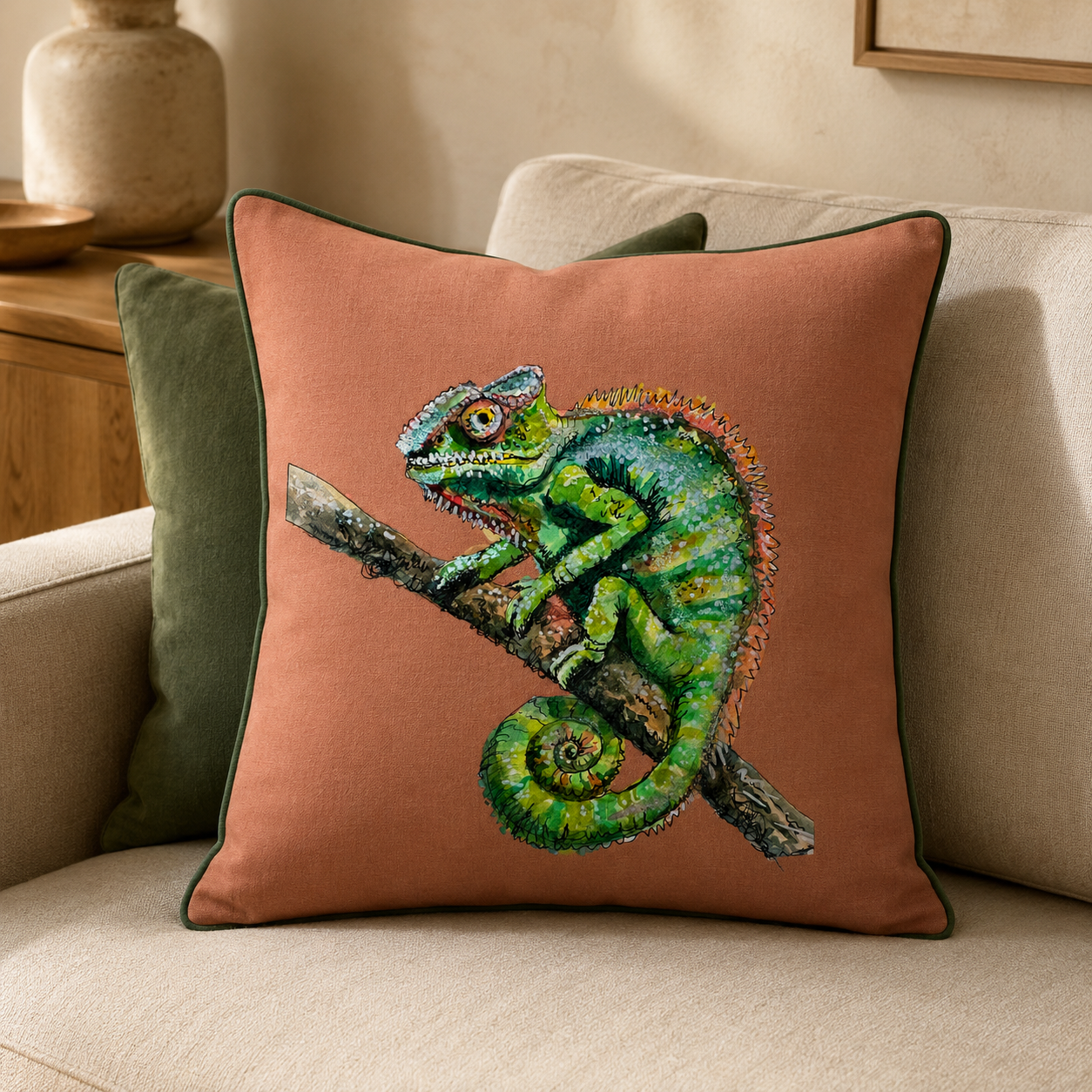 Decorative pillow with colorful, hand-painted original watercolor chameleon illustration sitting on a beige couch.