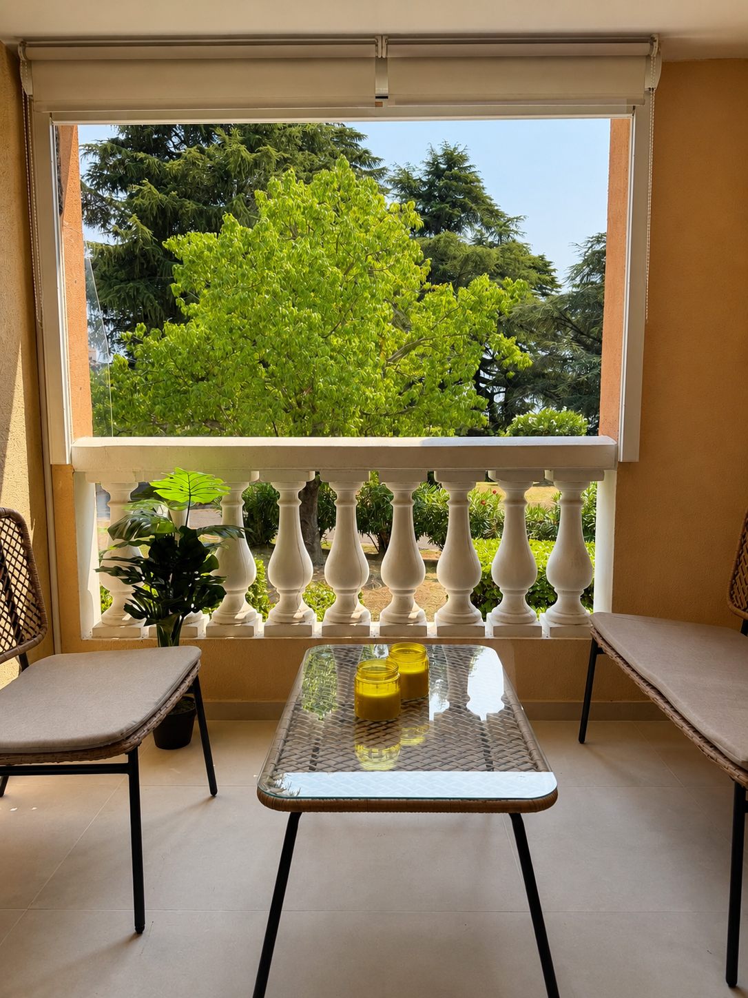 Balcon avec deux chaises, une table en verre et deux bougies jaunes, vue sur un arbre vert