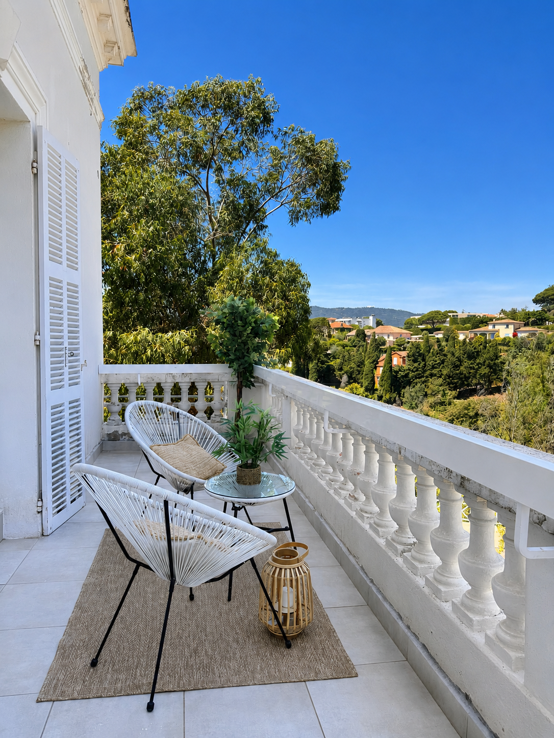 Balcon with white chairs, plants, and view of trees and houses under a blue sky