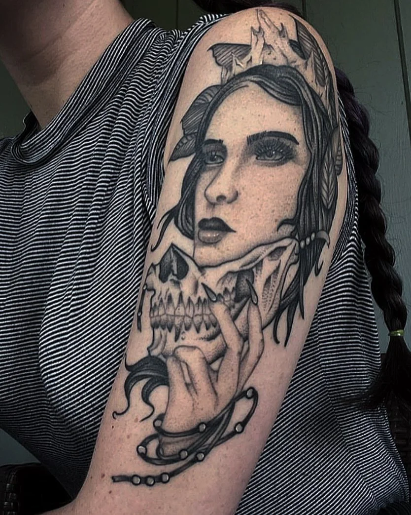 Tattoo of a woman's face with a skull and hand, surrounded by leaves and a butterfly on the shoulder.