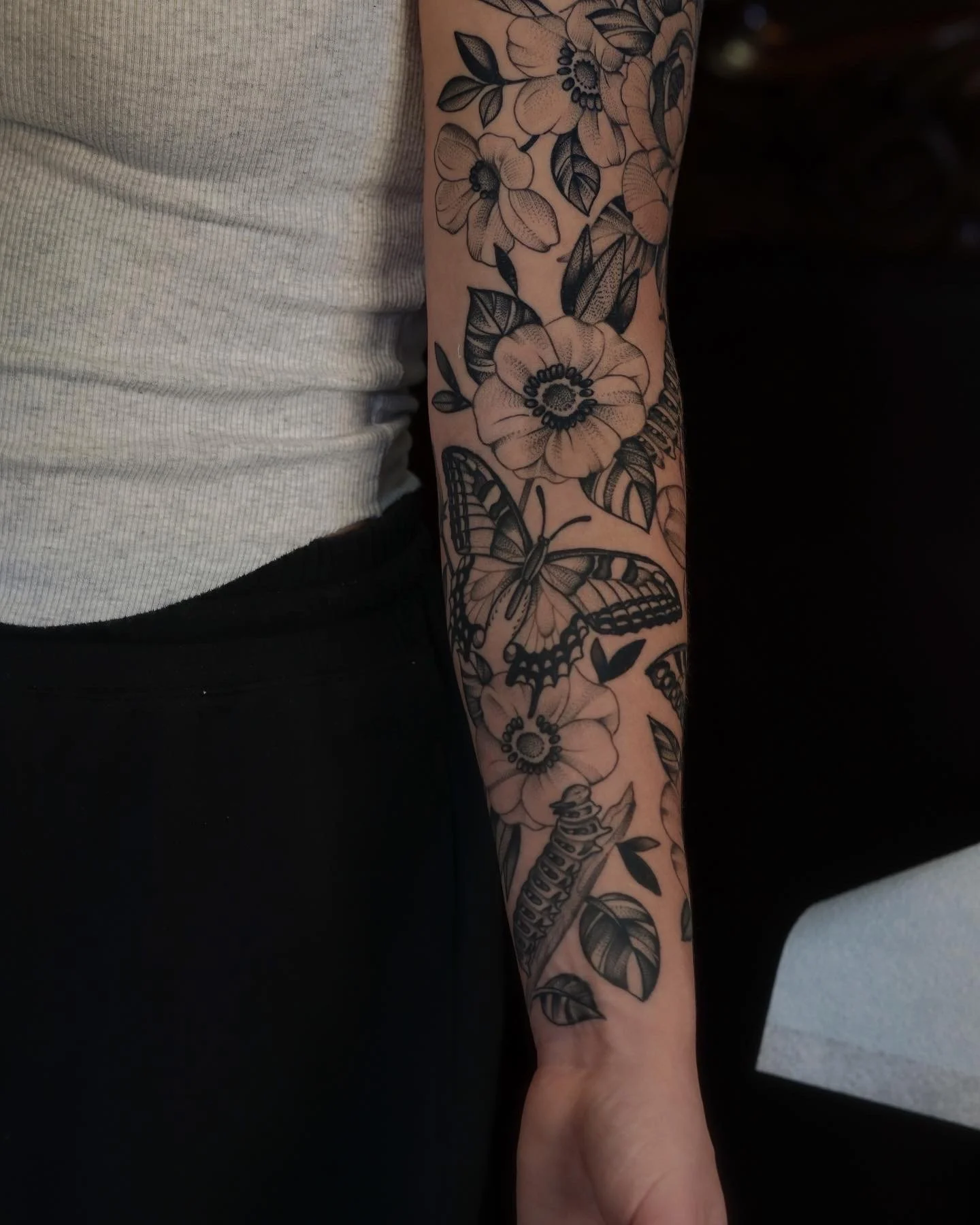 Tattooed arm featuring flowers, a butterfly, and a dragonfly.