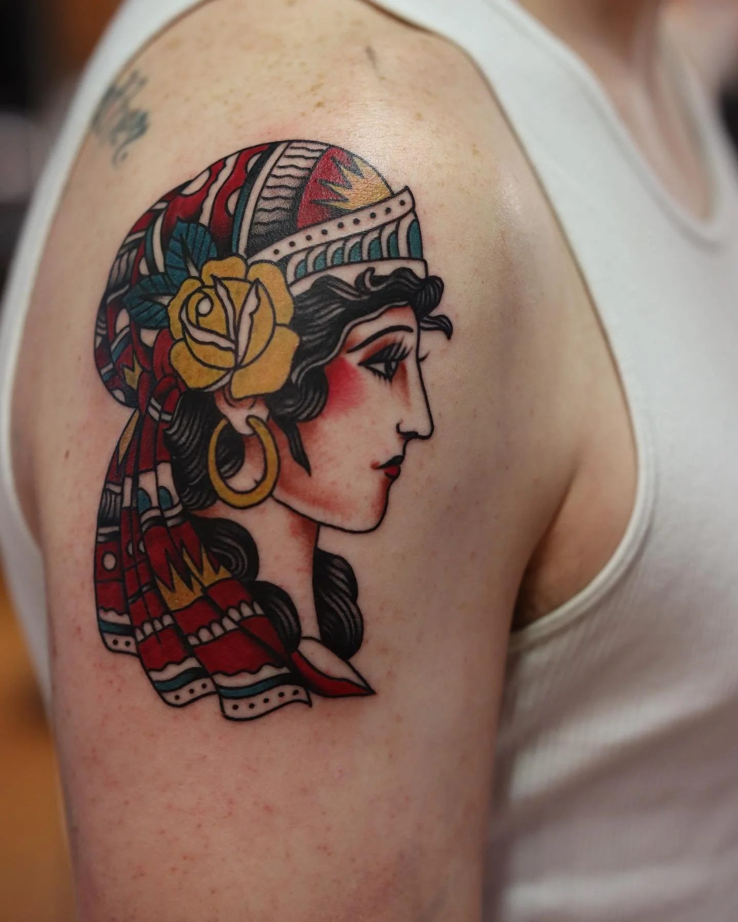 Colorful tattoo of a woman's profile with a floral headpiece and a decorative hat on upper arm.