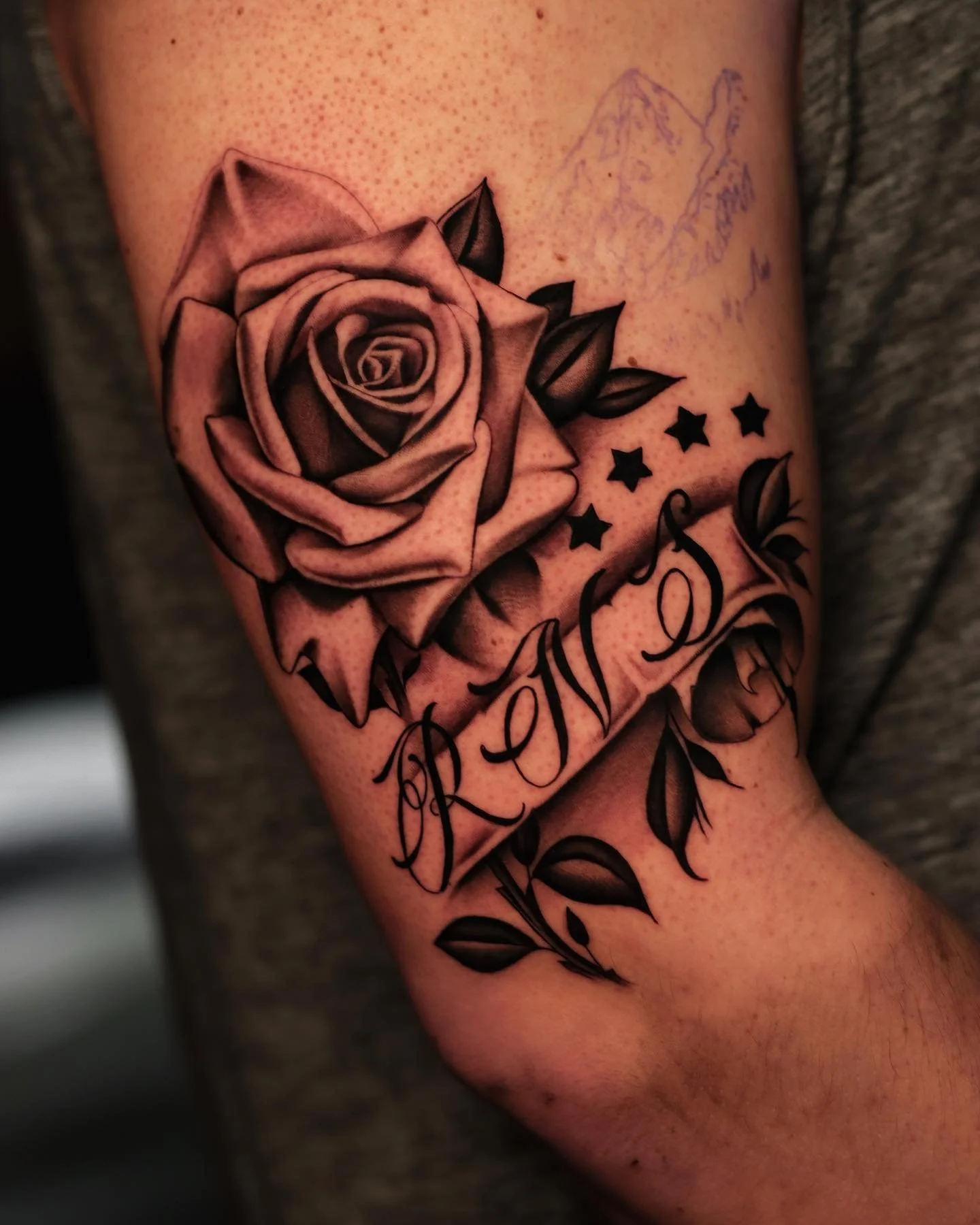 Tattoo of a detailed rose with leaves, stars, and the word 'Roses' on a person's arm.