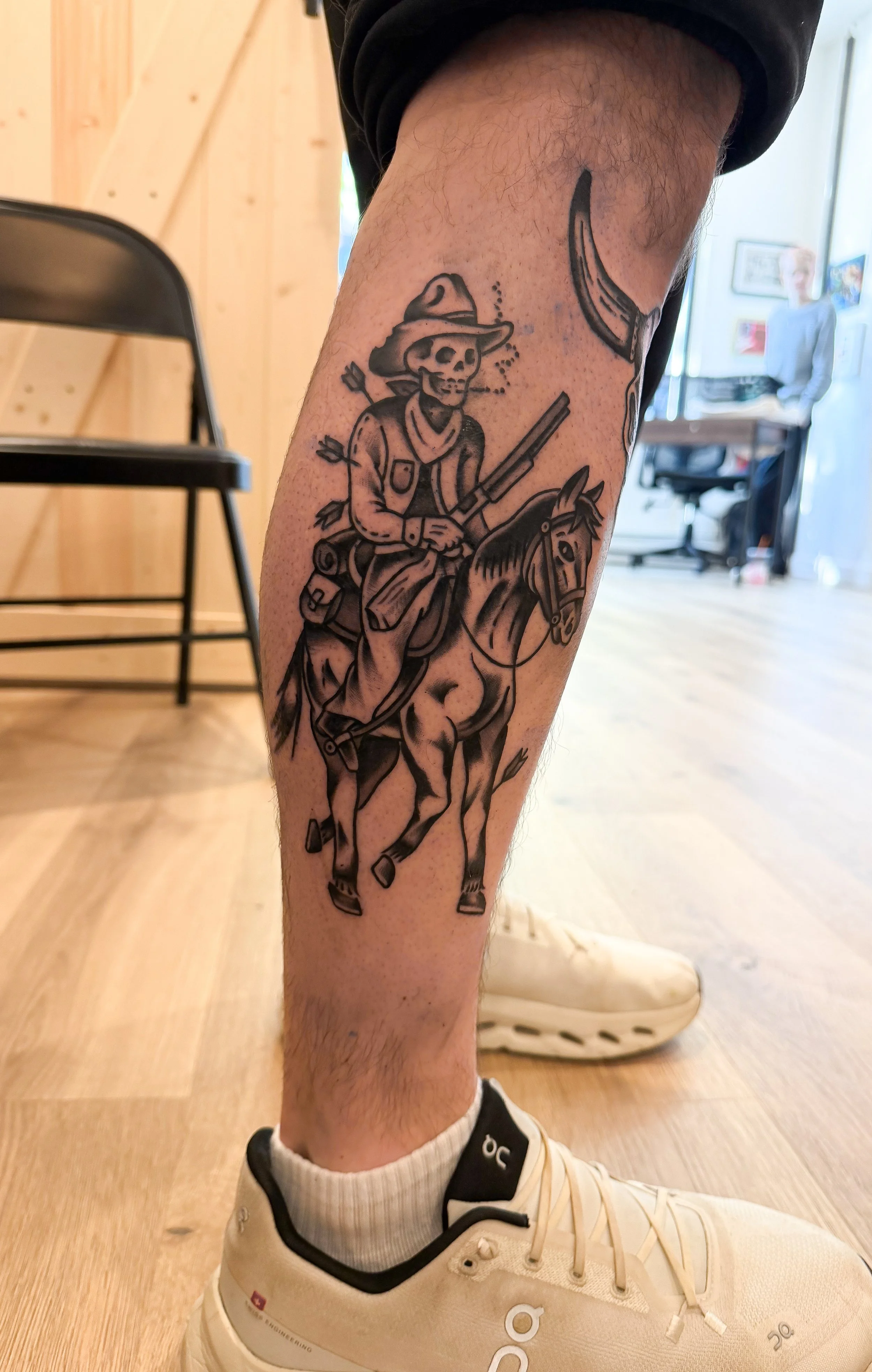 Tattoo of a skeleton cowgirl riding a horse on a person's lower leg.