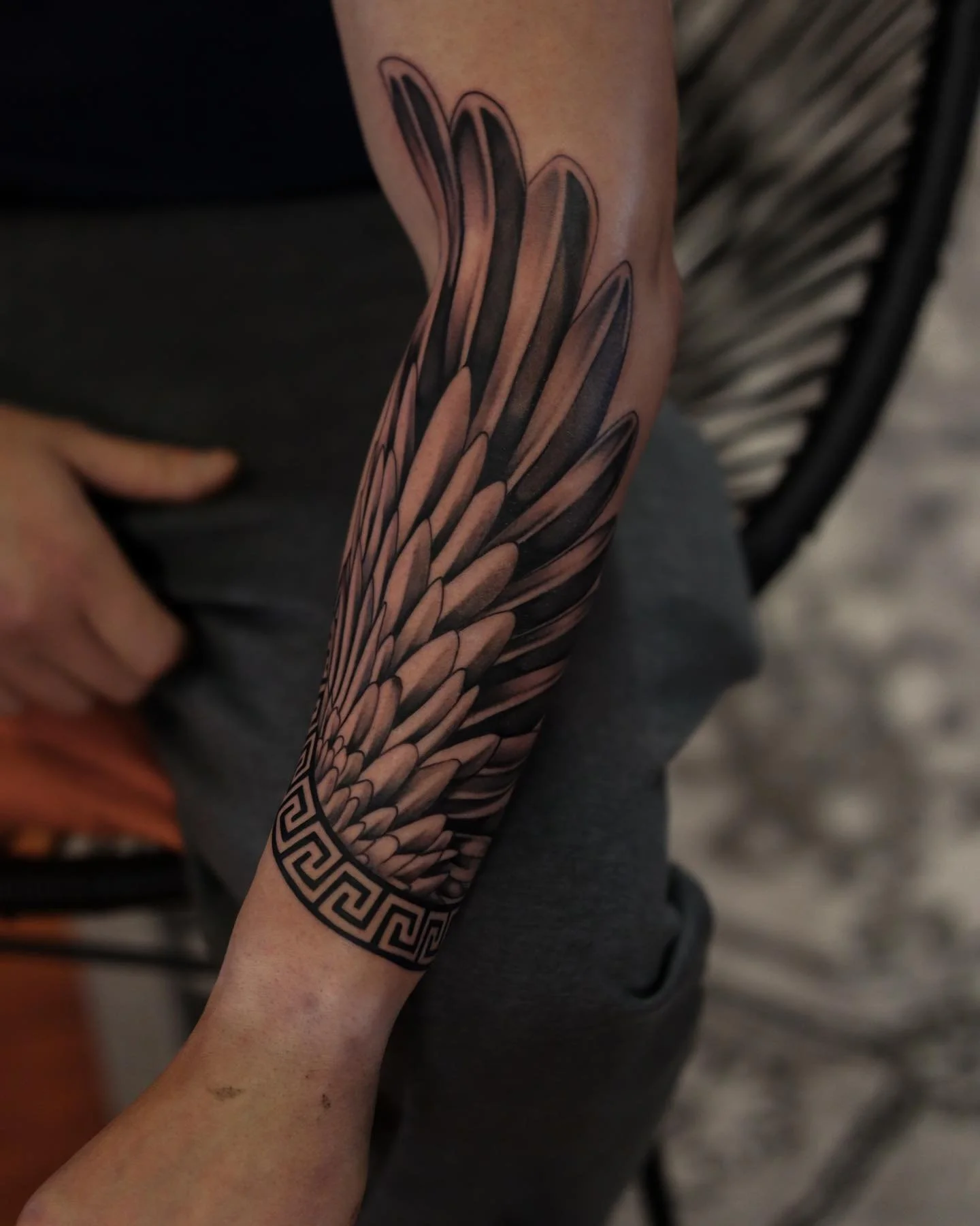 A person's arm with a detailed black and gray tattoo of a feather and geometric patterns.