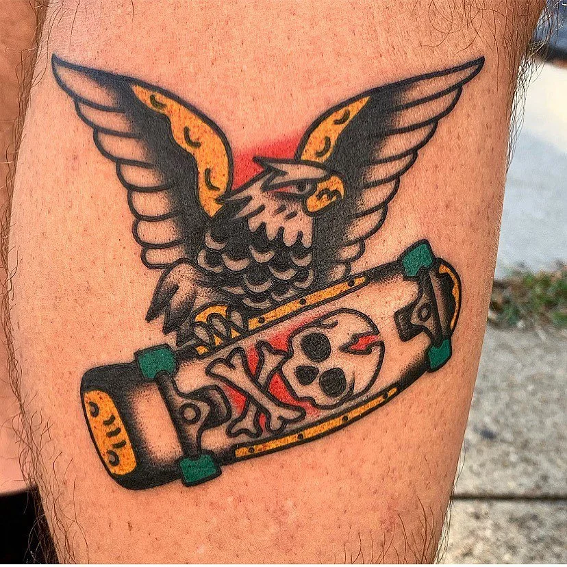 A colorful tattoo of a bird with outstretched wings holding a skateboard with a skull design on it.