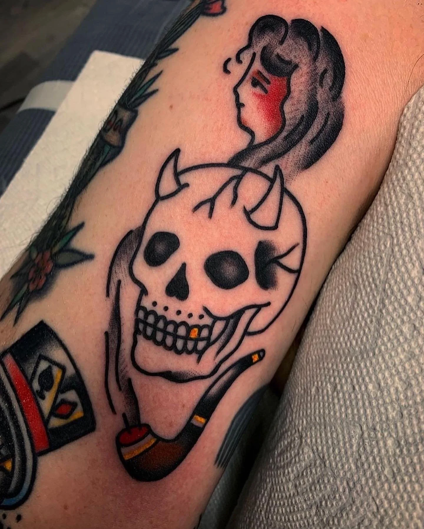 Tattoo of a skull with a diamond on its forehead and a hand holding the skull, on a person's arm.