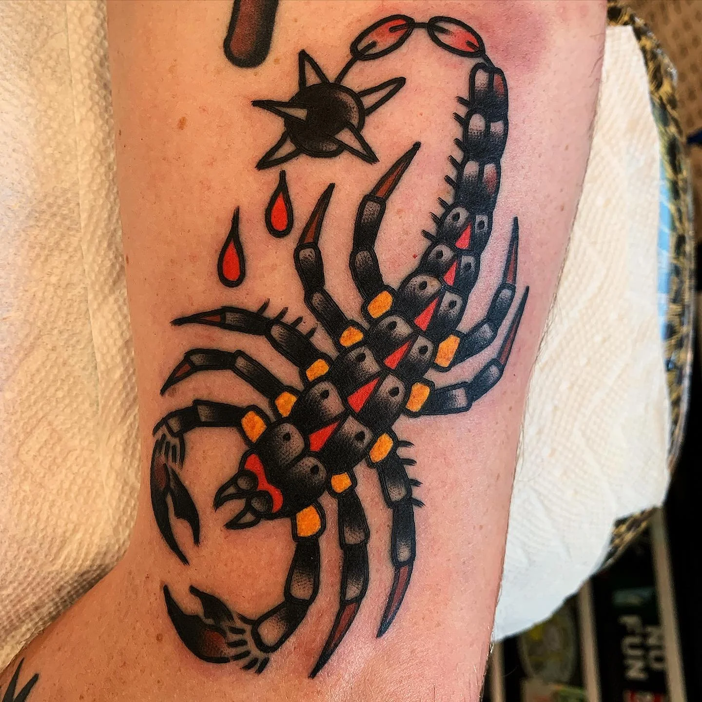 Colorful tattoo of a scorpion on skin with black, red, and yellow details, and its claws and tail extended.