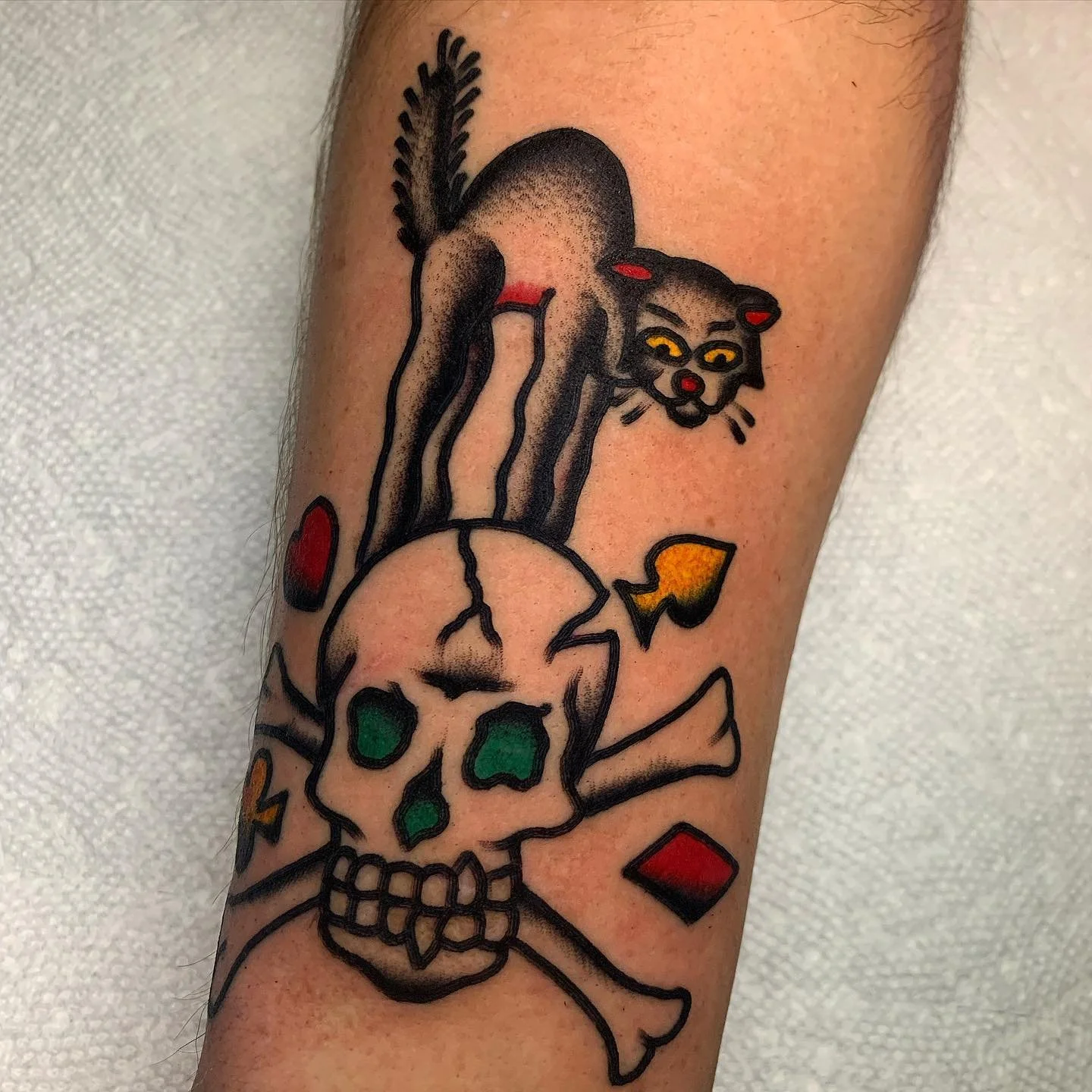 Tattoo of a stylized skull with green eye sockets, topped by a dog head with yellow eyes, red ears, and a red nose, on a person's arm.
