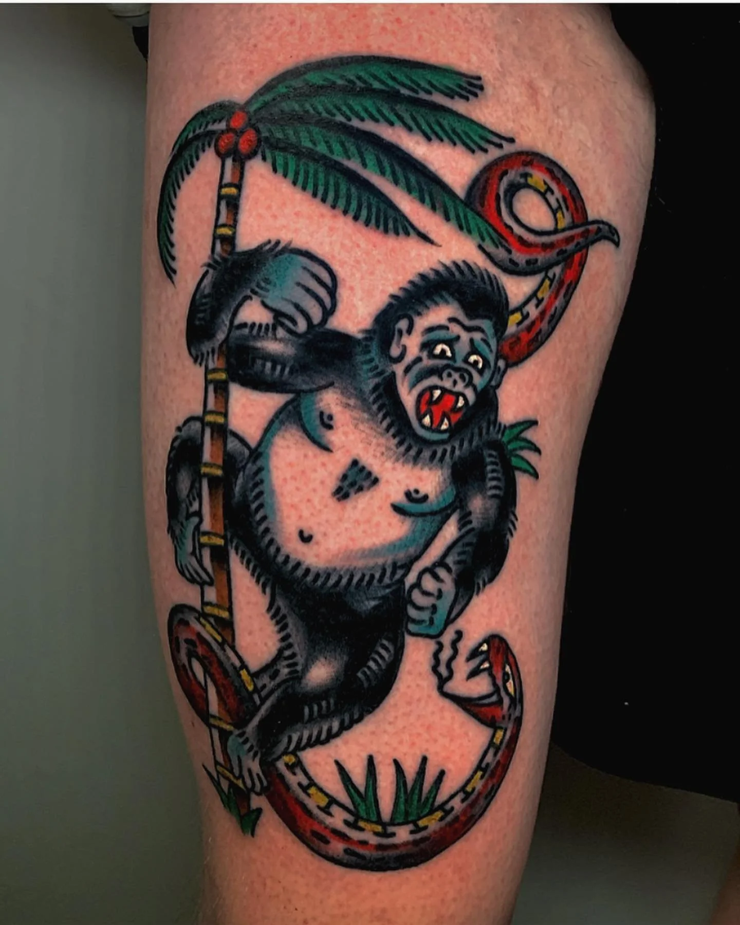 A tattoo of a monkey holding a colorful snake and a palm tree on a person's arm.