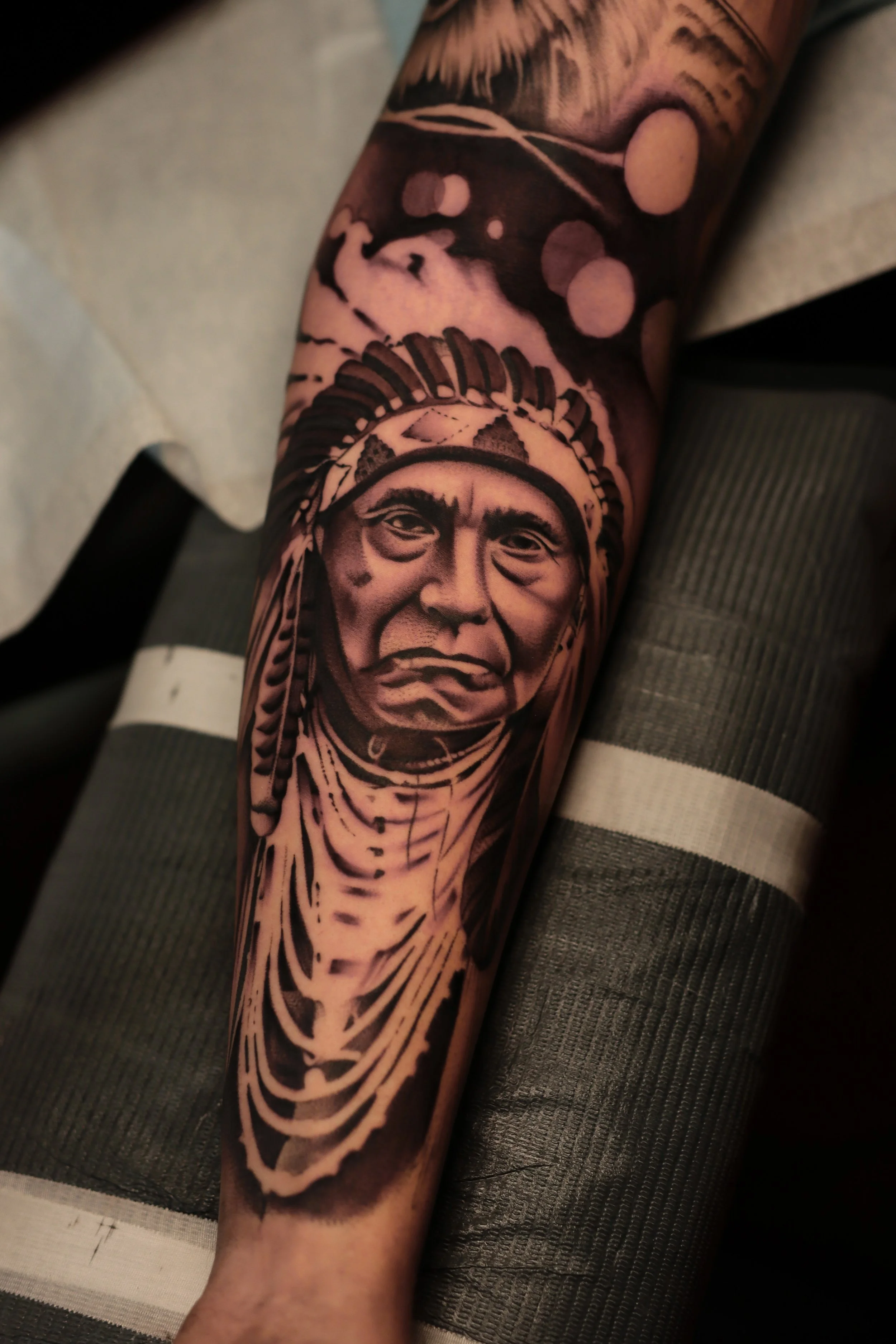 A tattoo of a Native American chief wearing a headdress on a person's forearm.