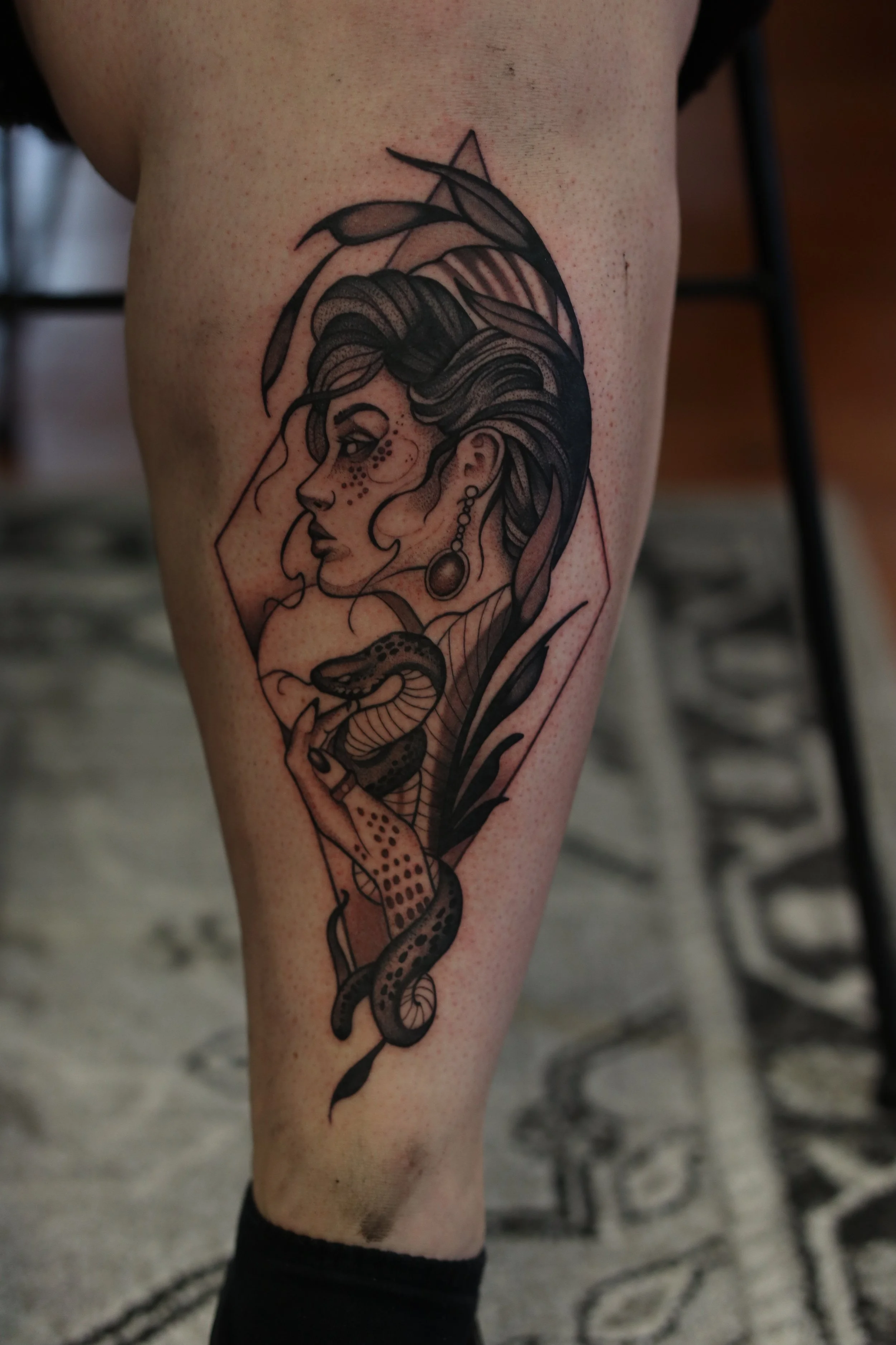 Tattoo of a woman with long hair and snake wrapped around her arm on a person's thigh.
