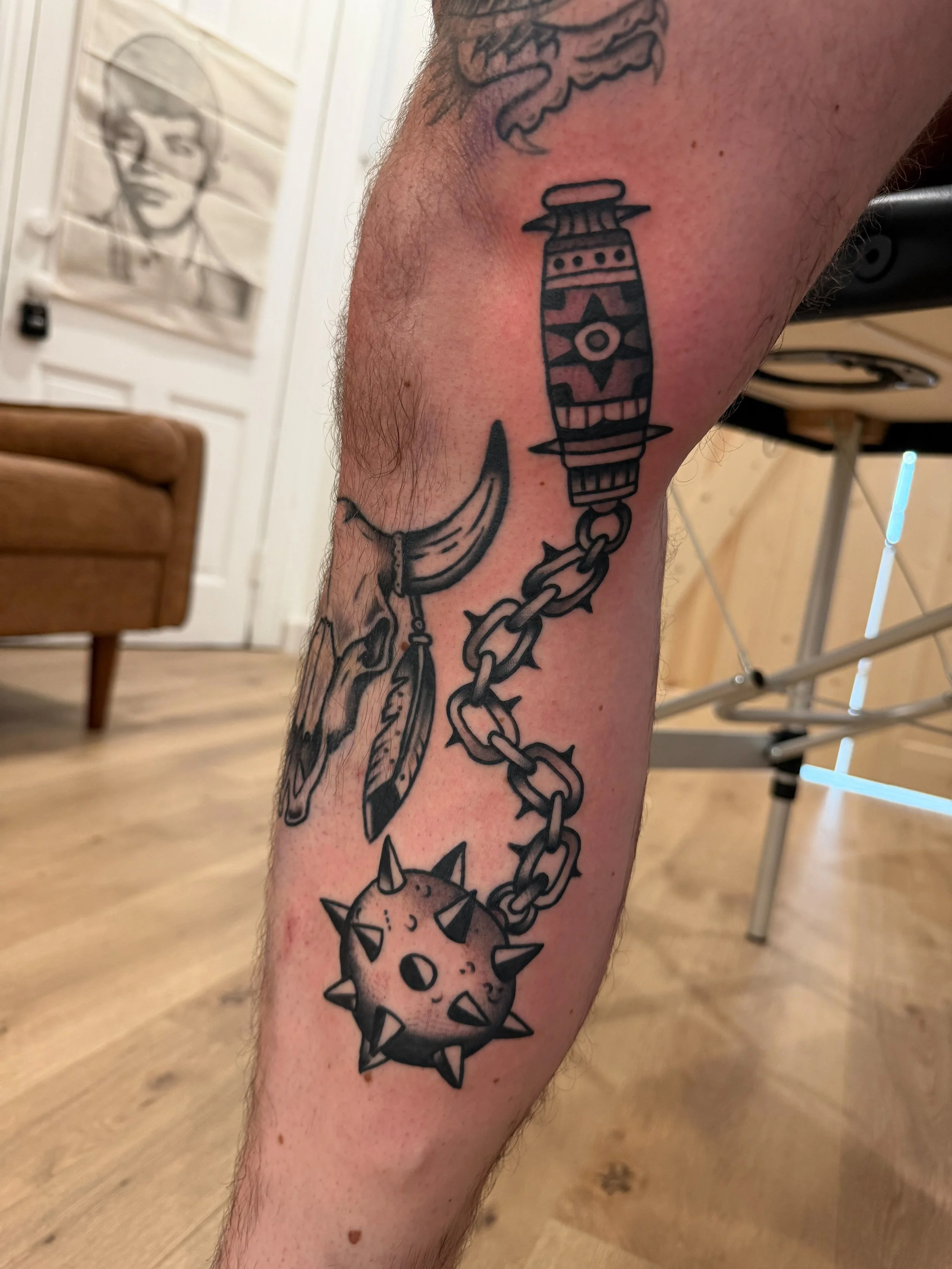 Tattoo of a spiked mace ball connected to a chain on a person's thigh.