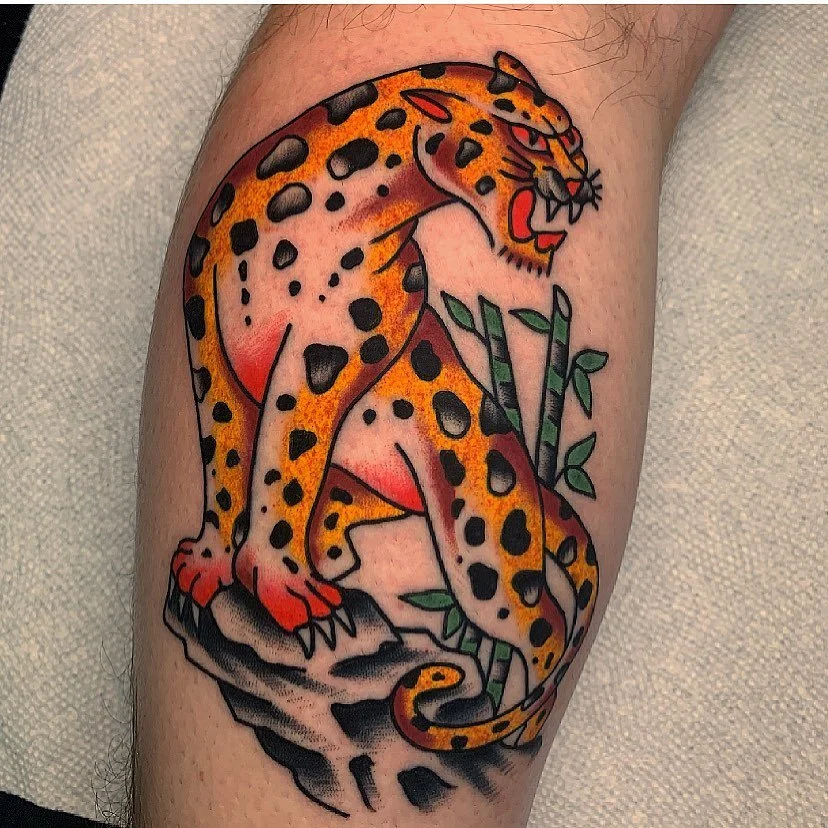 Tattoo of a leaping jaguar with spotted fur, perched on rocks and surrounded by green bamboo stalks with leaves.