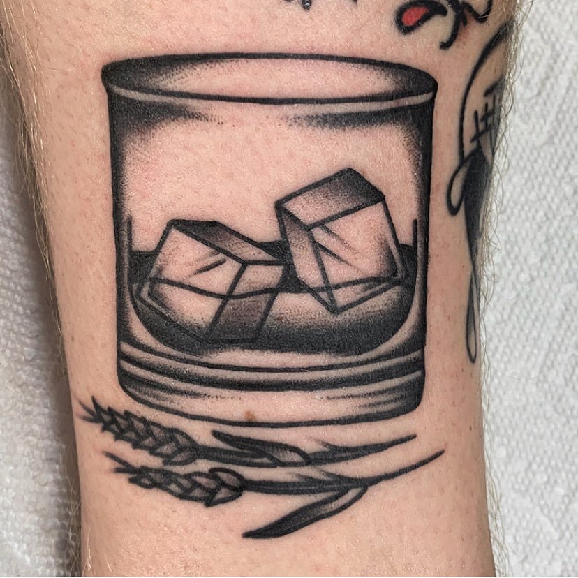 Tattoo of a glass with ice cubes and a straw, with grains of wheat beneath it.