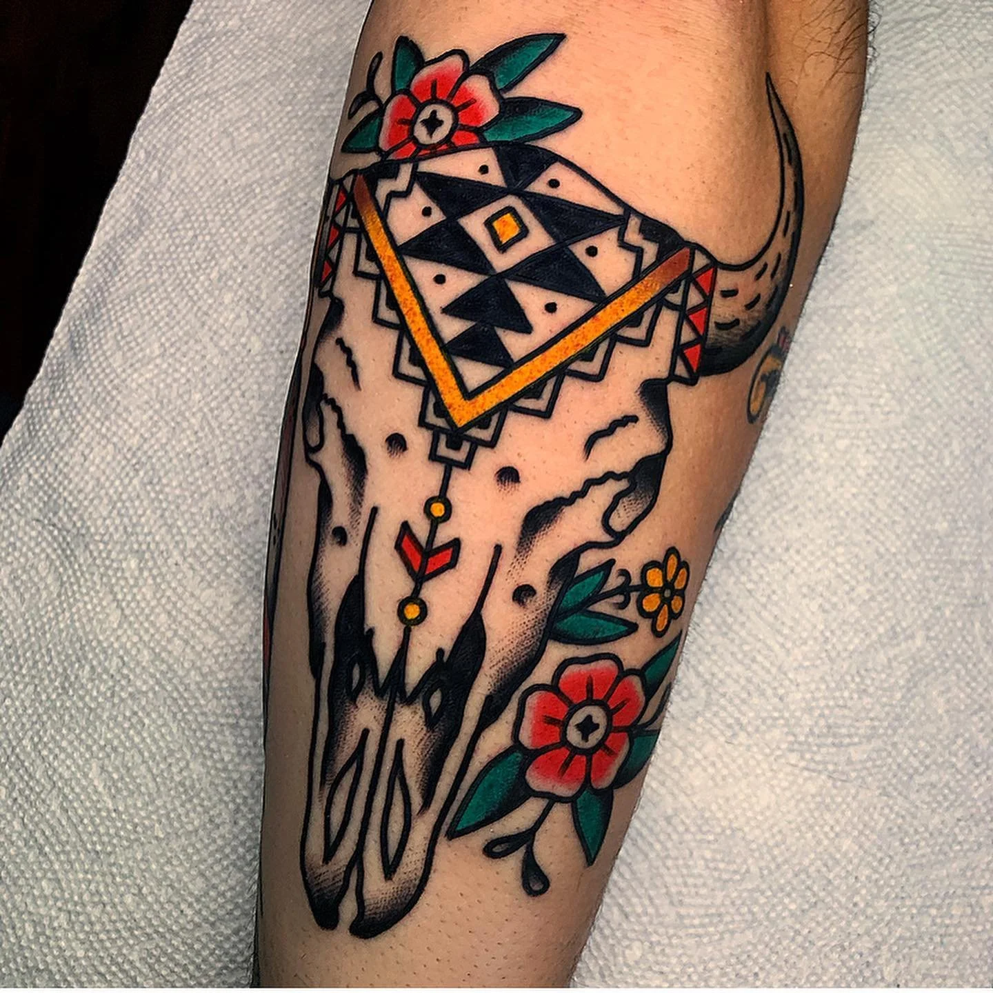 Tattoo of a deer skull adorned with a geometric diamond-shaped design and floral accents on a person's arm.