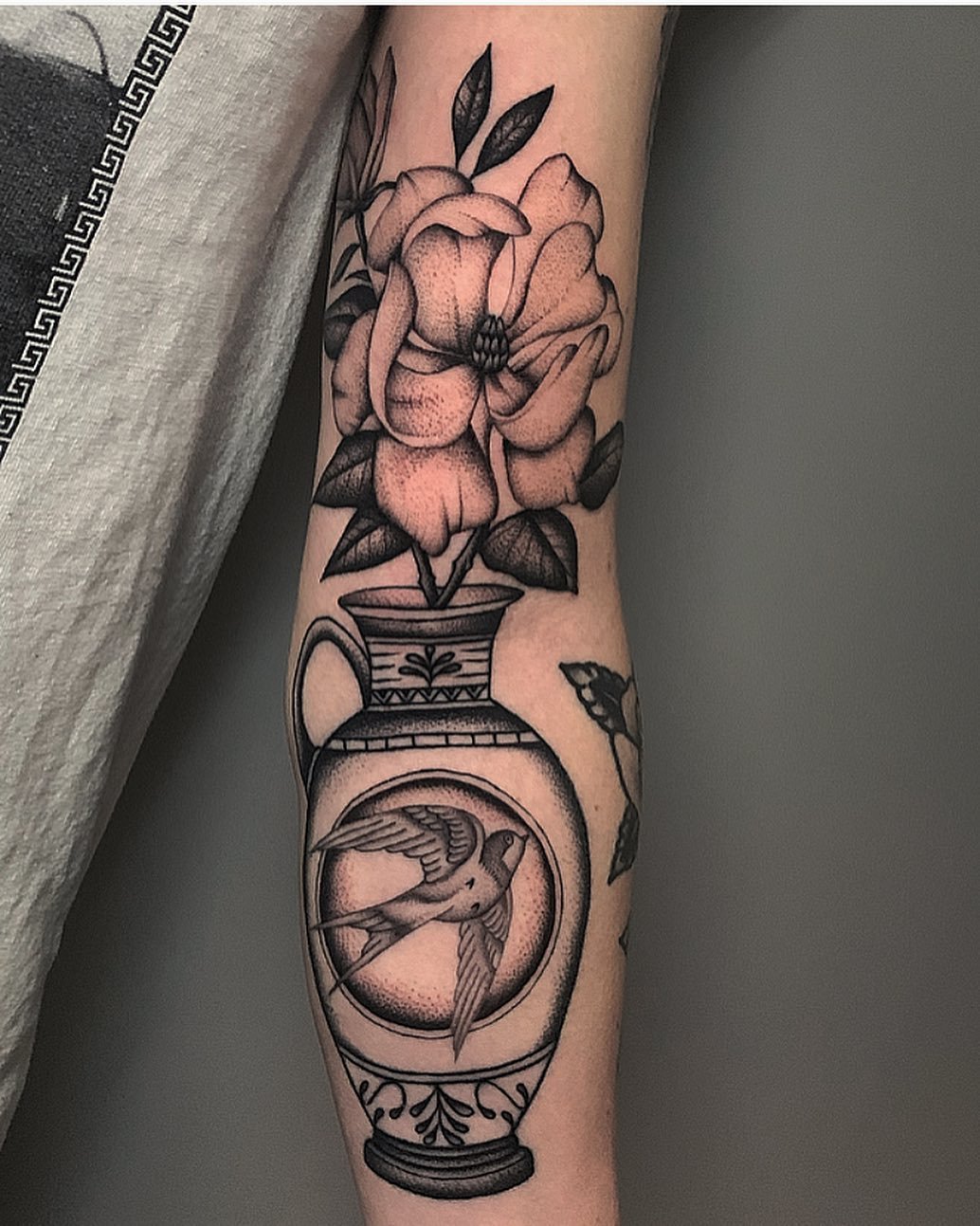 Tattoo of a large flower in a vase with a hummingbird in a circular design on the lower part of the tattoo.