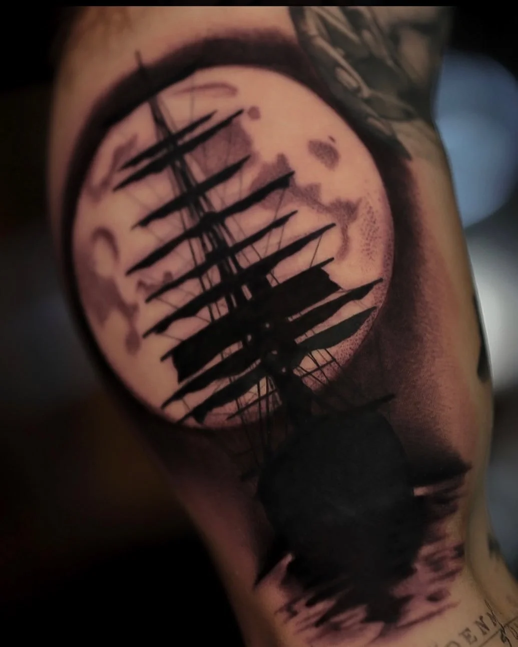 Tattoo of a rocky landscape scene with a sunset or moon in the sky, framed by a circular border, and featuring a ship's silhouette in the foreground.