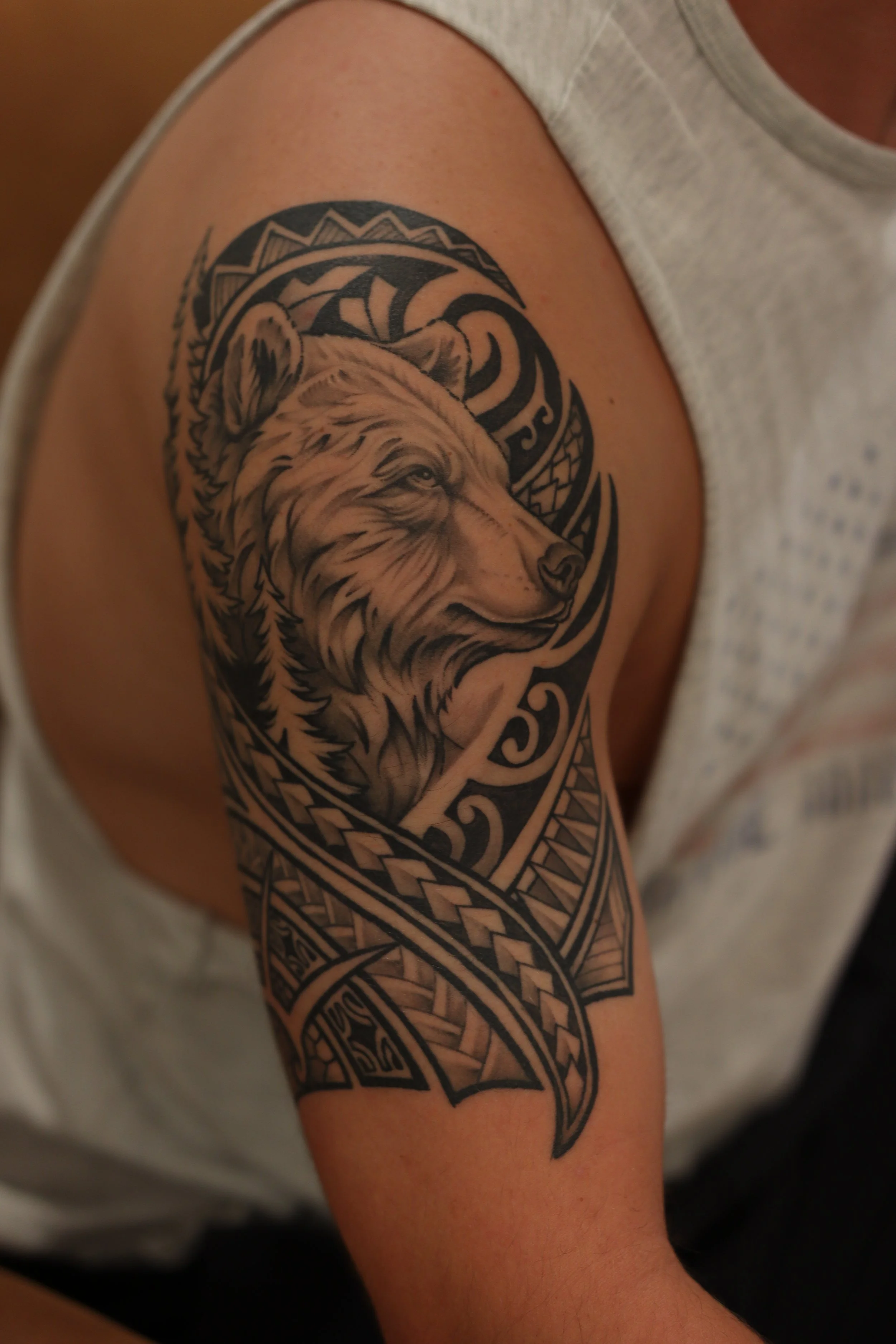 Close-up of a person's upper arm with a detailed black and gray tattoo of a wolf's head and tribal patterns surrounding it.