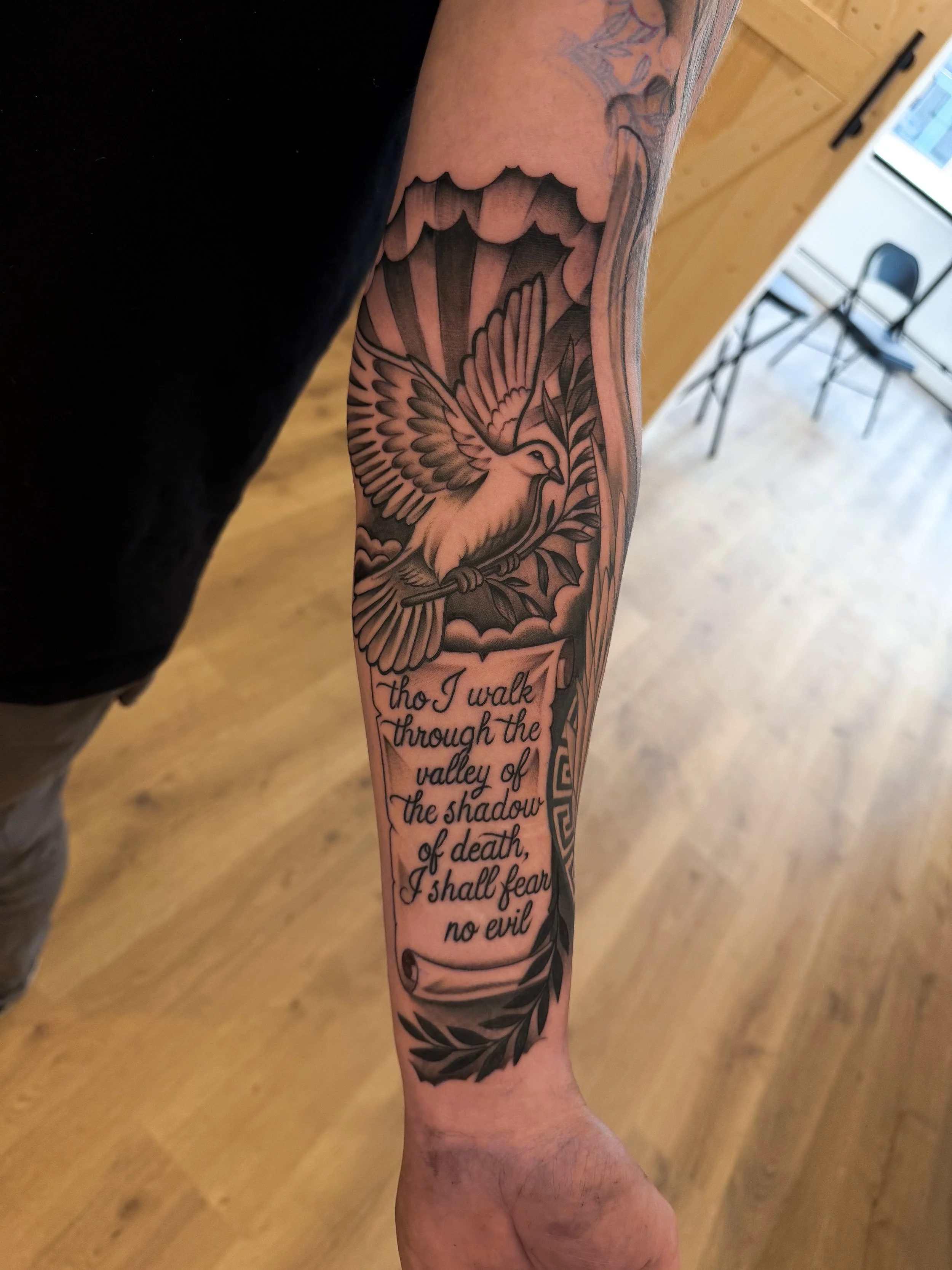 Tattoo of a dove holding an olive branch, with a background of stylized sun rays and clouds, and text below reading a quote about walking through the valley of shadow of death and fearing no evil.
