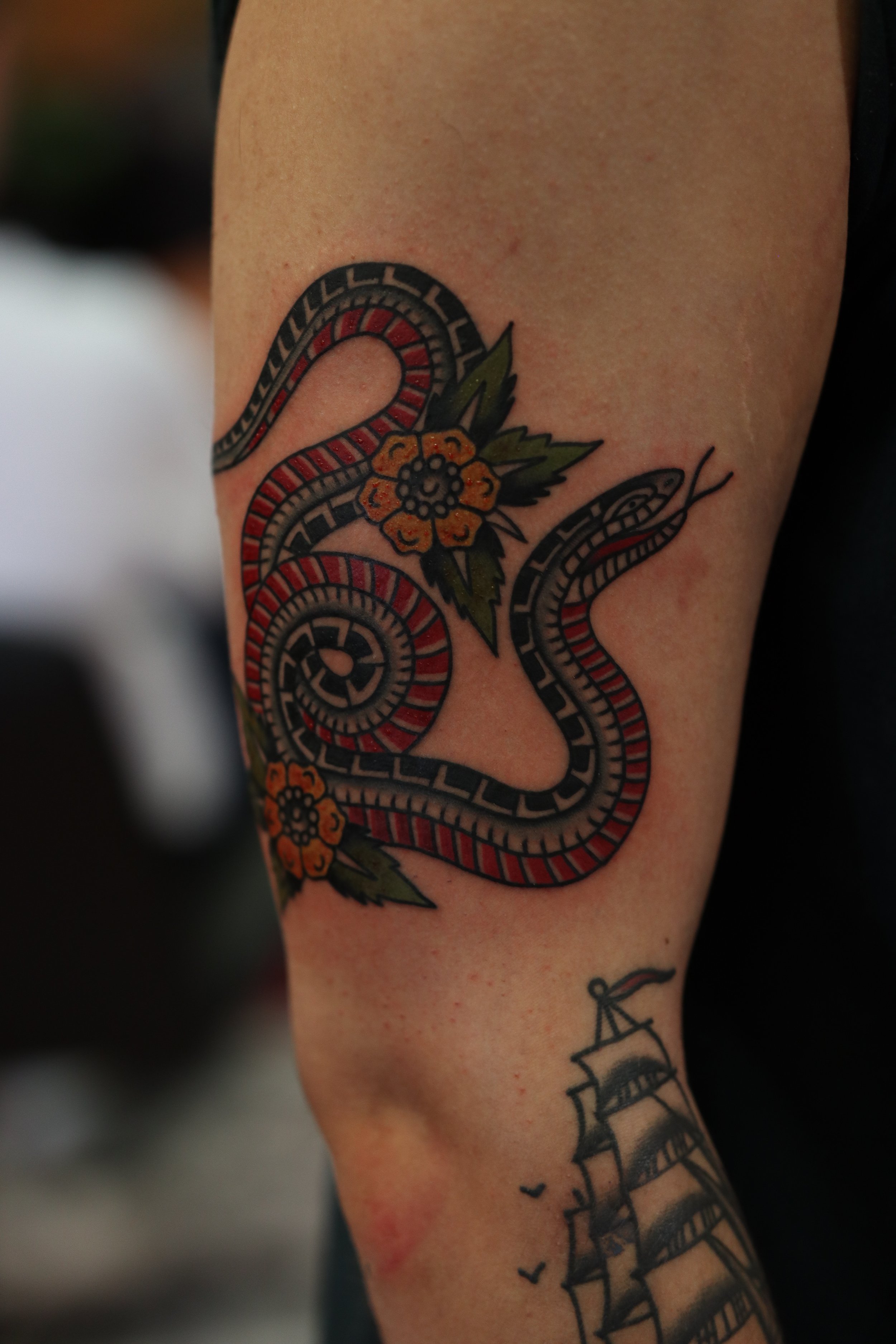 A tattoo of a snake intertwined with colorful flowers on a person's arm.