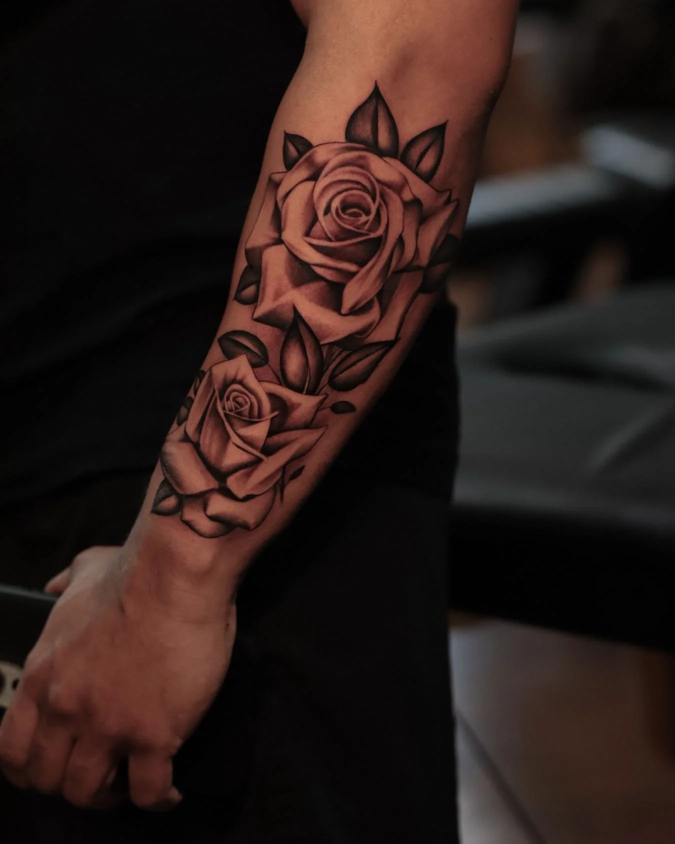 A tattoo of two realistic pink roses with dark leaves on a person's forearm.