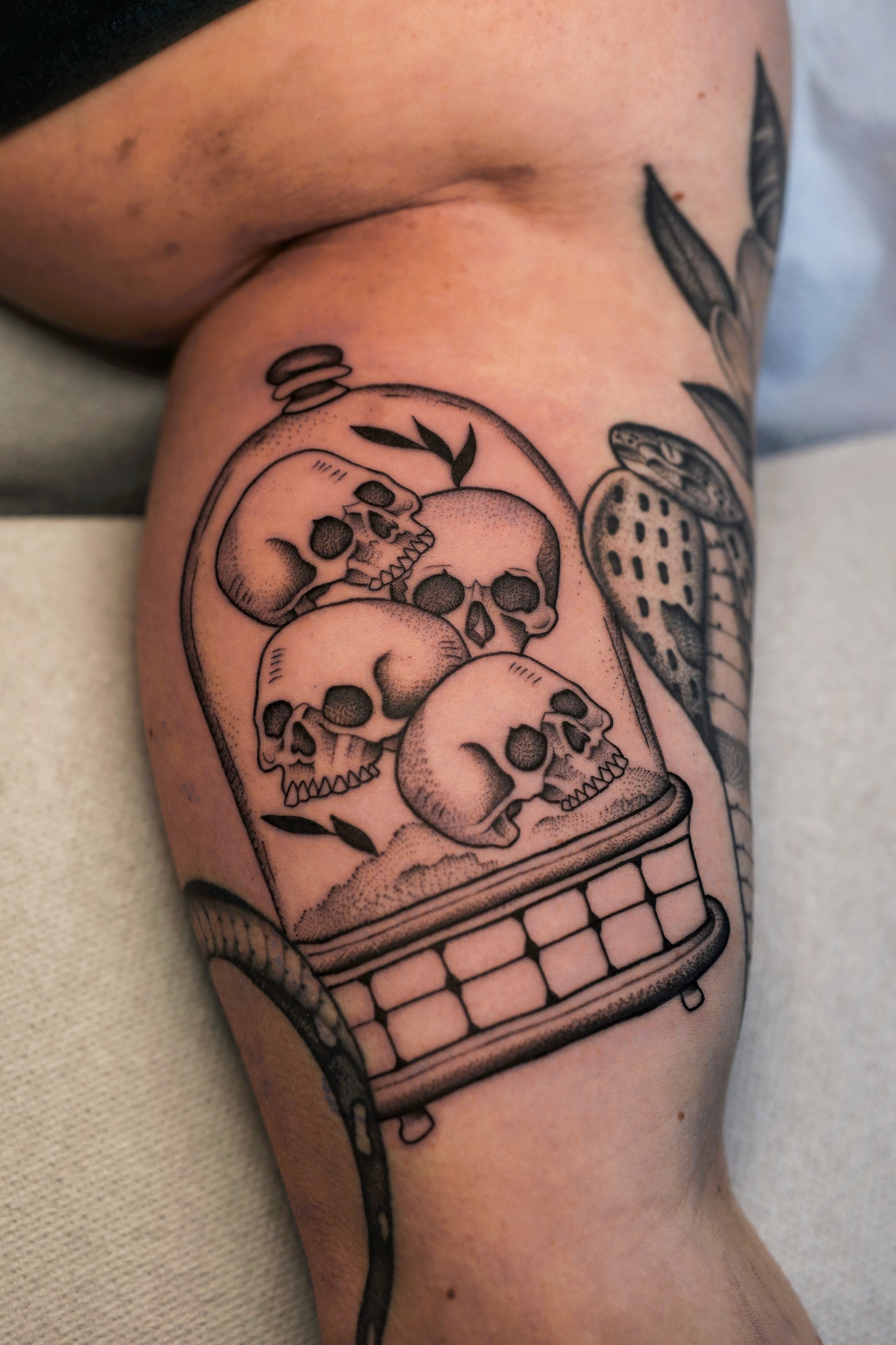 Tattoo of a glass filled with skulls and flowers on a person's upper arm.