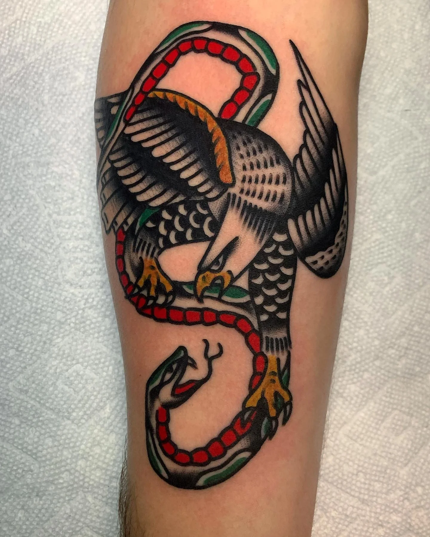 Traditional tattoo of a snake with a coiled body, incorporating red, green, yellow, and black colors, on a person's arm.