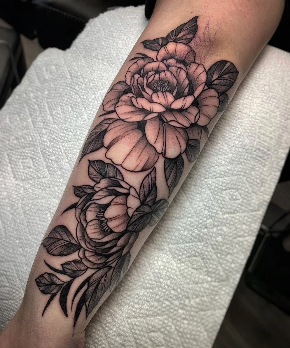 Black and gray floral tattoo on a person's forearm featuring large blooming flowers with detailed petals and leaves.