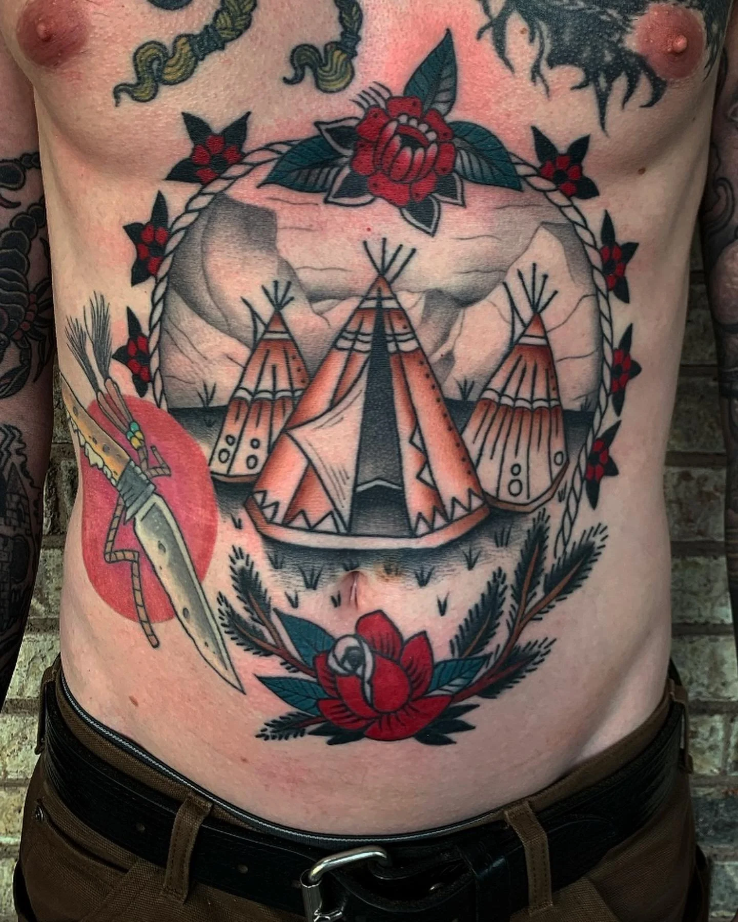 Tattoo art on a person's chest featuring a dreamcatcher with feathers and a rose, surrounded by other floral designs.