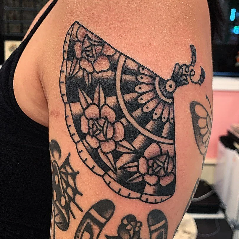 Tattoo of a decorative fan with floral and geometric patterns on a person's upper arm.