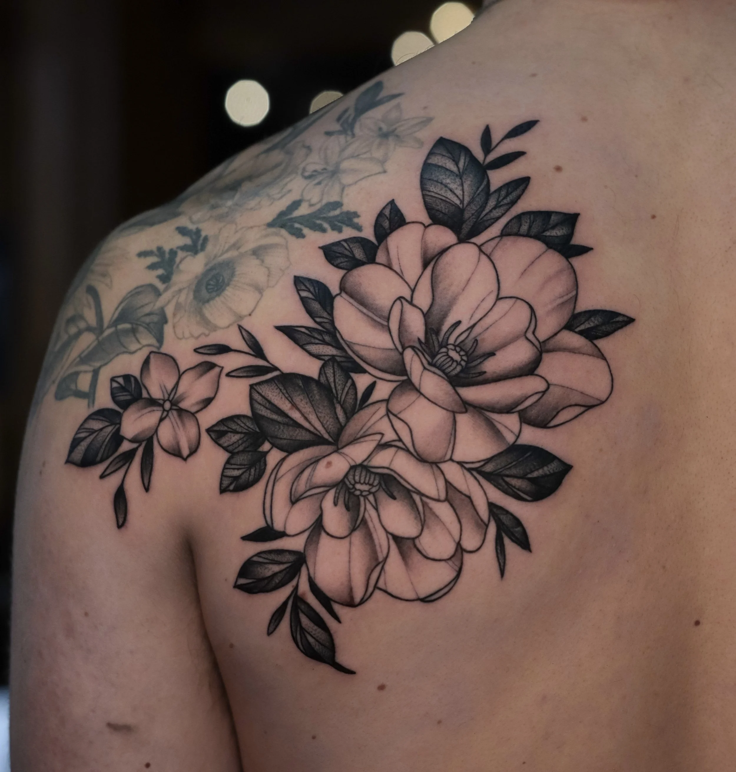 Close-up image of a person's shoulder with a detailed floral tattoo in black ink.