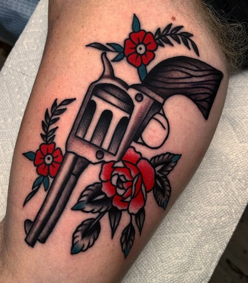 A tattoo of a revolver surrounded by red flowers and black leaves.