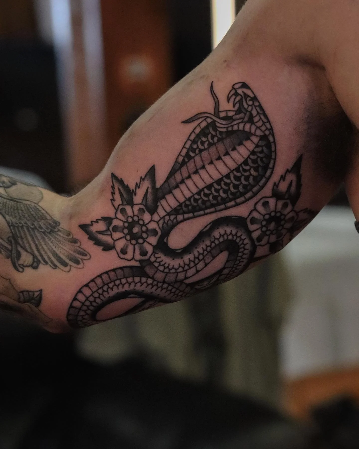 Tattoo of a snake intertwined with flowers on a person's arm and shoulder.