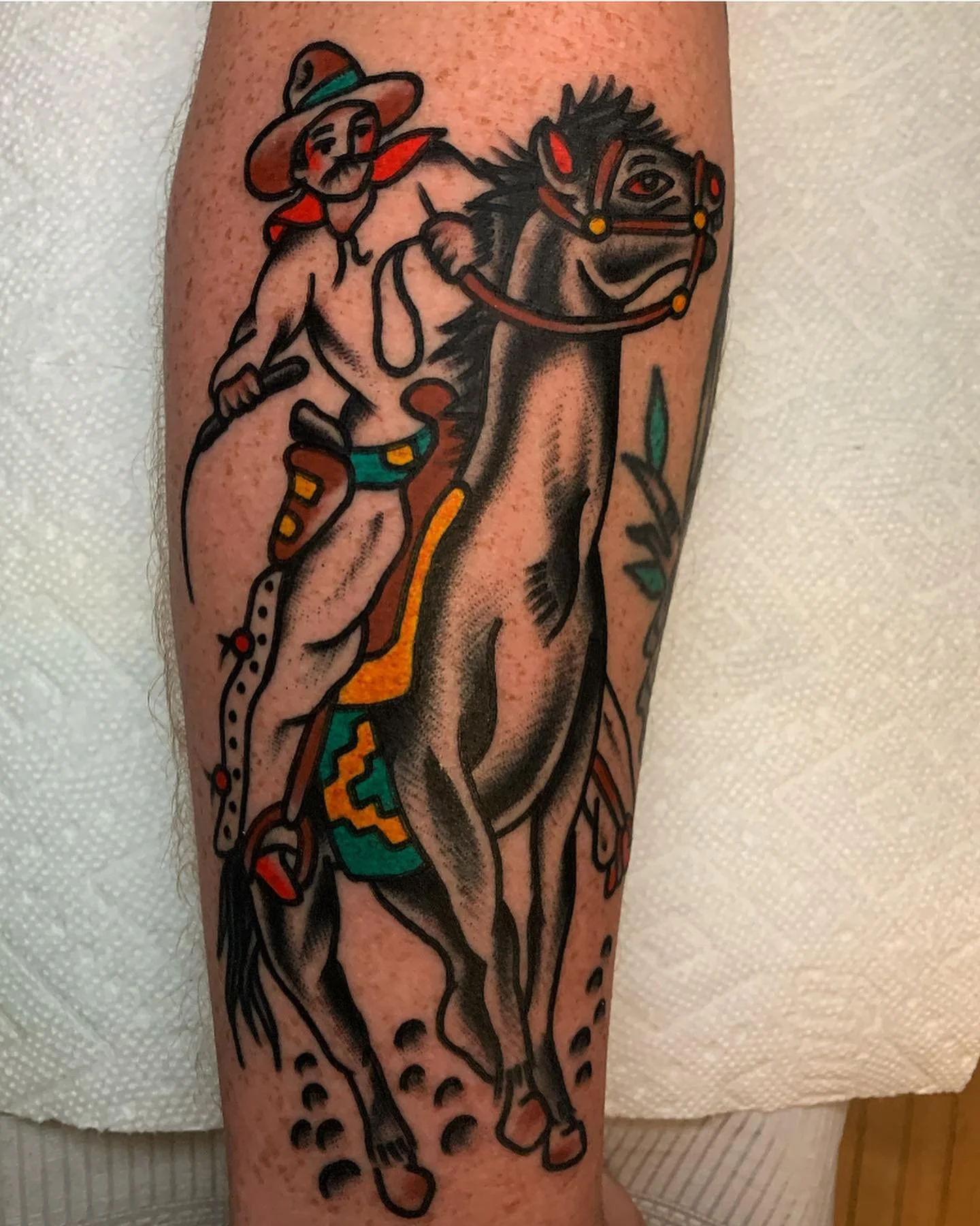 Tattoo of a woman riding a horse, with cacti and southwestern motifs, outlined in black with colorful accents, on a person's arm.