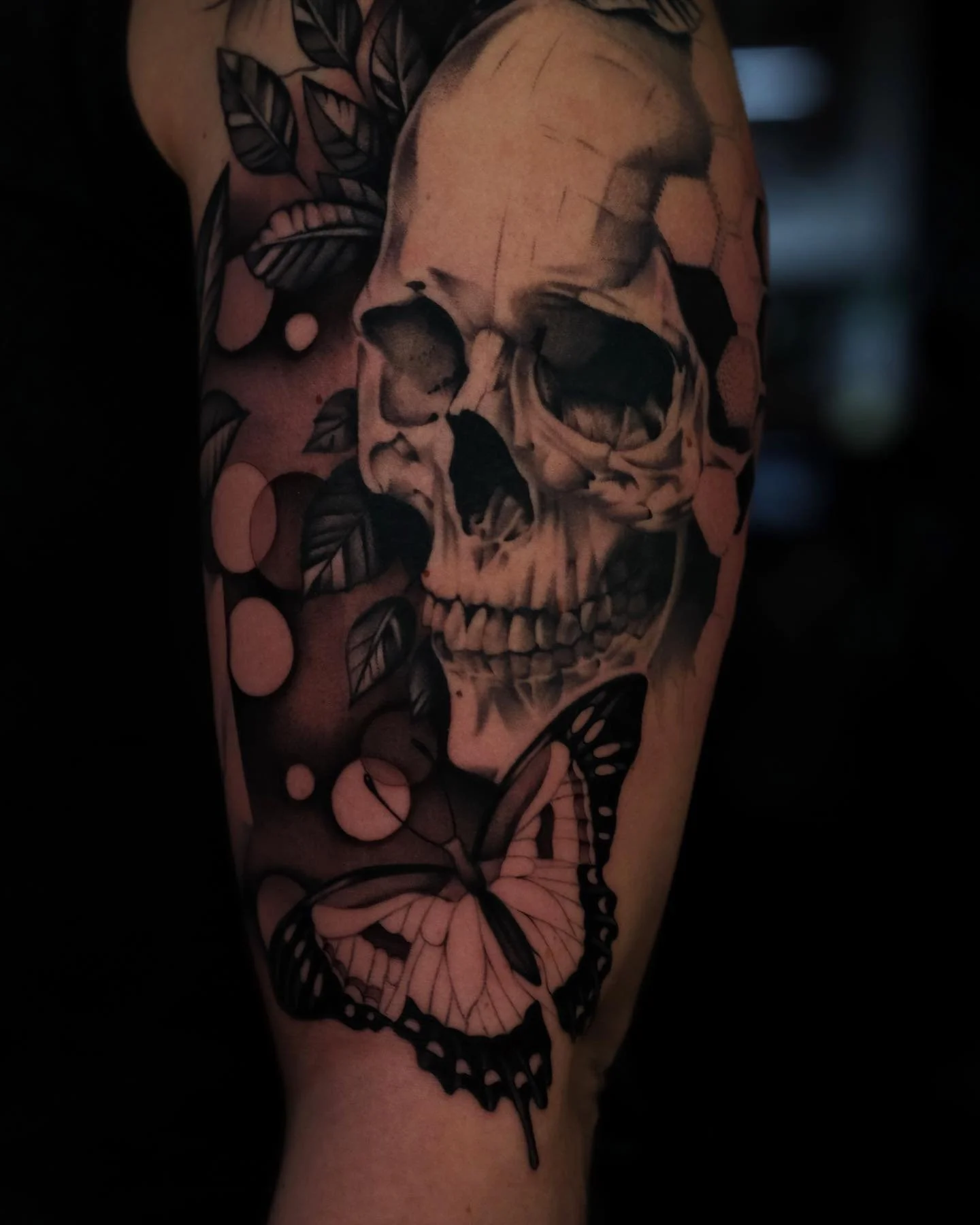 A tattoo of a human skull surrounded by flowers and leaves on a person's arm.