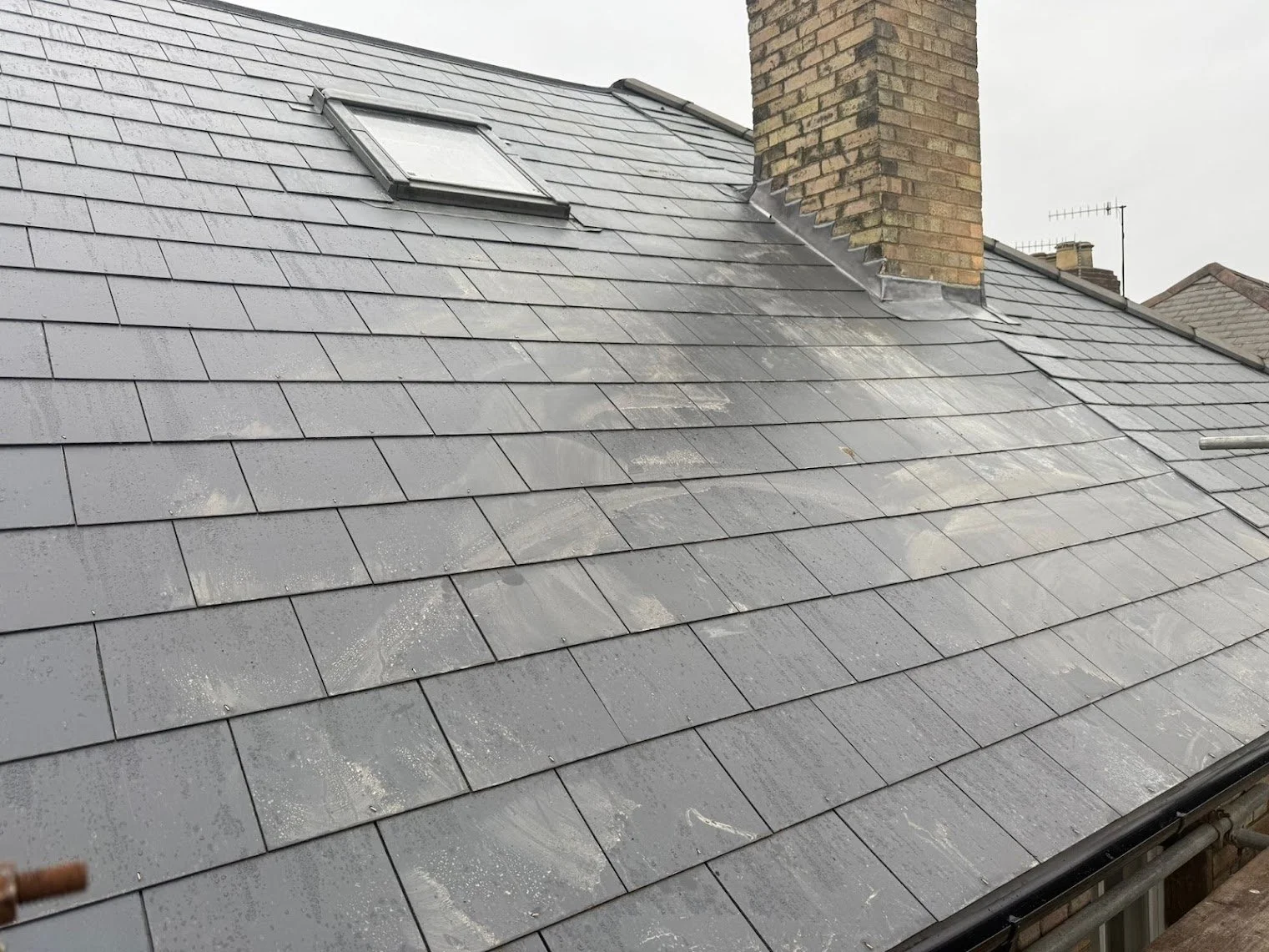 A roof with dark asphalt shingles, a skylight, a brick chimney, and a cloudy sky in the background.