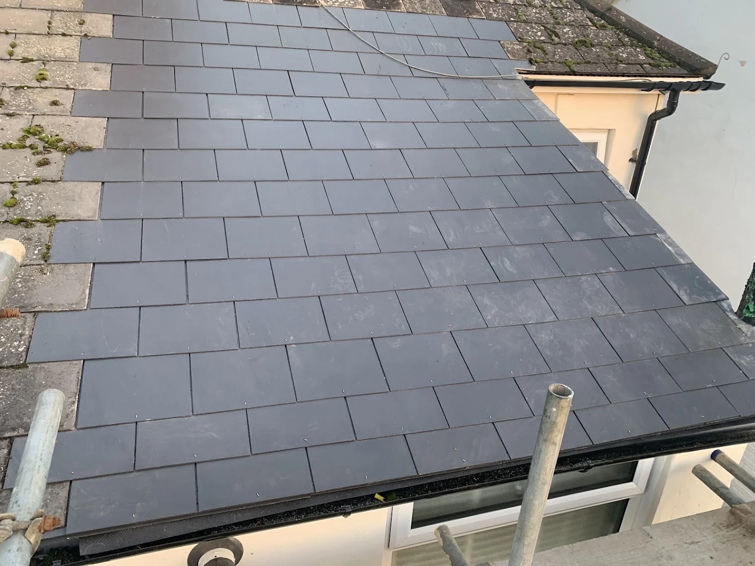 Newly installed dark gray slate roof shingles on the roof of a building, with scaffolding visible at the bottom of the image.