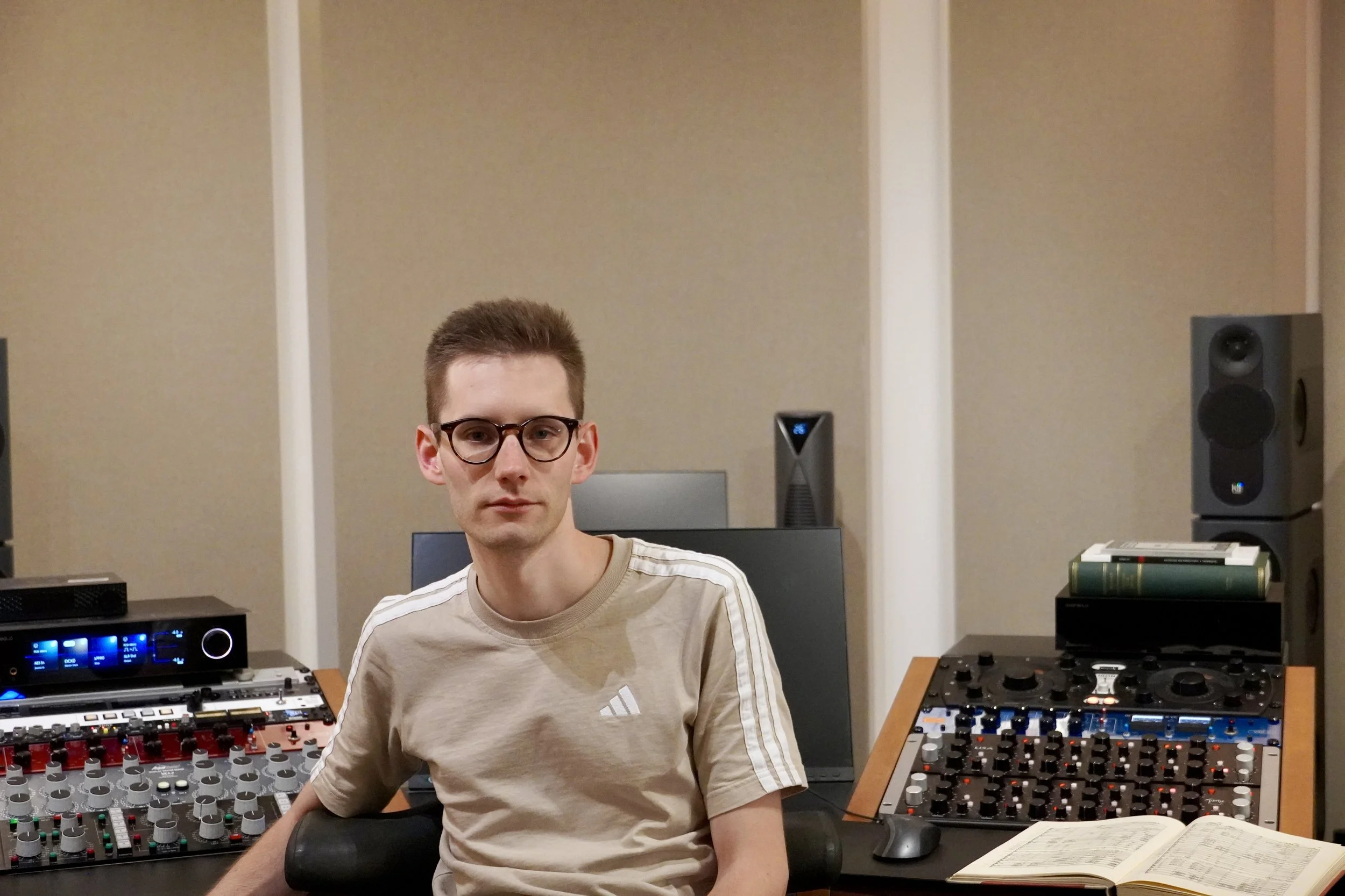 Tonmeister Malte Waag sitzt in einem Tonstudio vor einem Mischpult, umgeben von Audio-Equipment, einschließlich Lautsprechern und einem Computer.