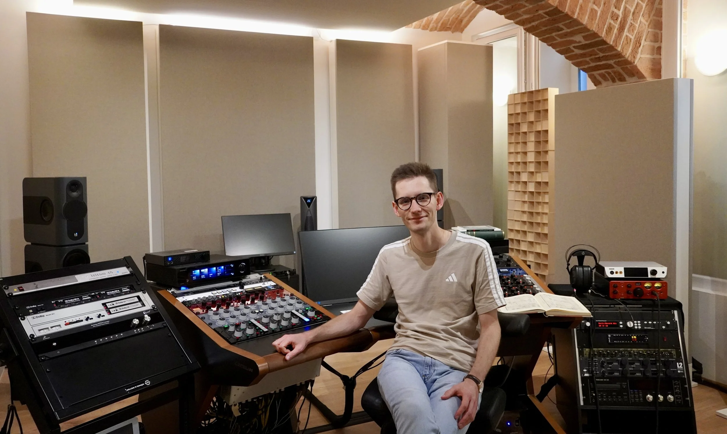 Tonmeister Malte Waag sitzt in einem Tonstudio vor einem Mischpult, umgeben von professioneller Studioausrüstung und Partituren.