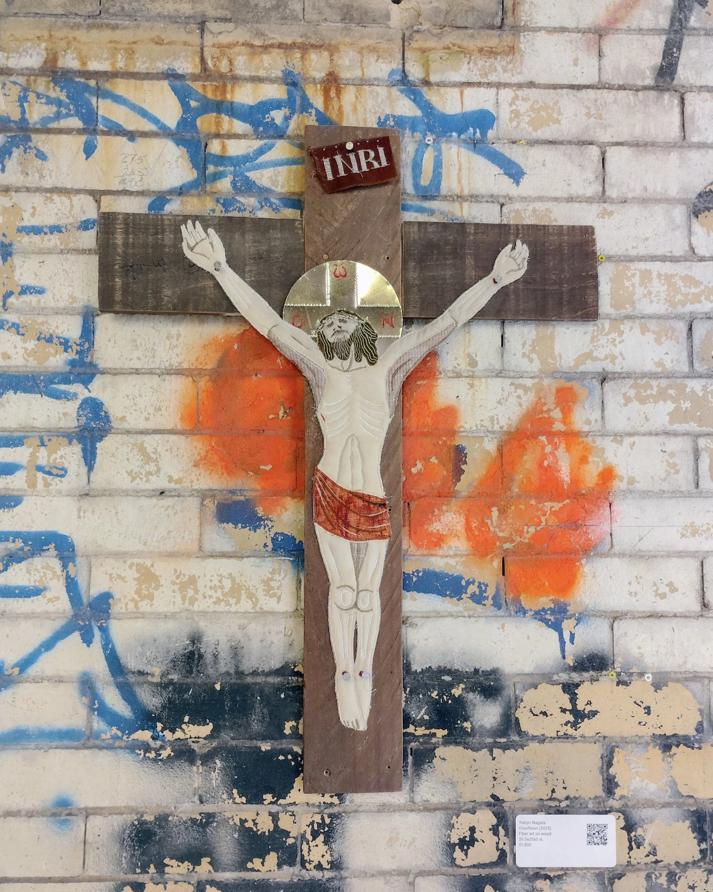 "Crucifixion" 2025, 26.5" x 20.5". Recycled fabric and tin on recycled cross shaped wood. A picture as installed at Unmoored/Unbound exhibition at Powerhouse Arts by Brooklyn Waterfront Artists Coalition on 2026.