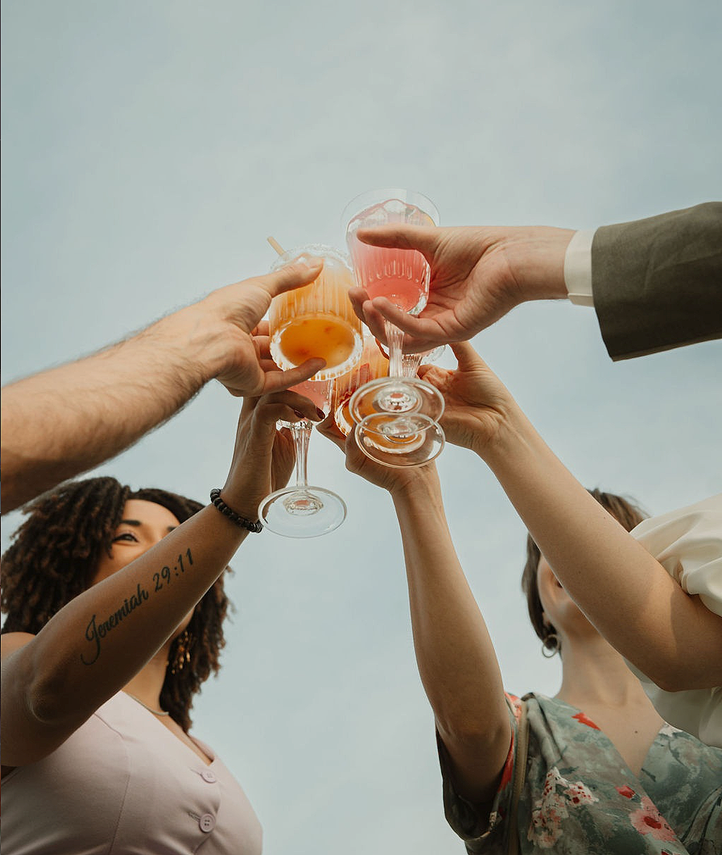 Multiple people raising their glasses in a toast outdoors against a cloudy sky, celebrating.